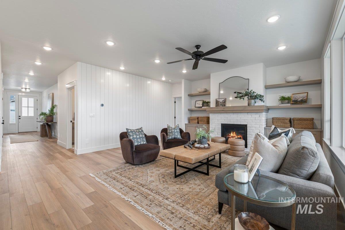 Living room featuring light wood-type flooring, a brick fireplace, a ceiling fan, and recessed lighting