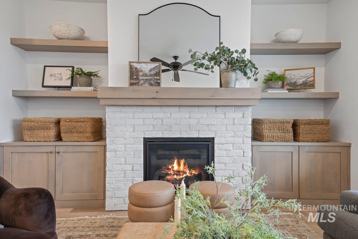 Living area with a brick fireplace, wood finished floors, a ceiling fan, and built in shelves