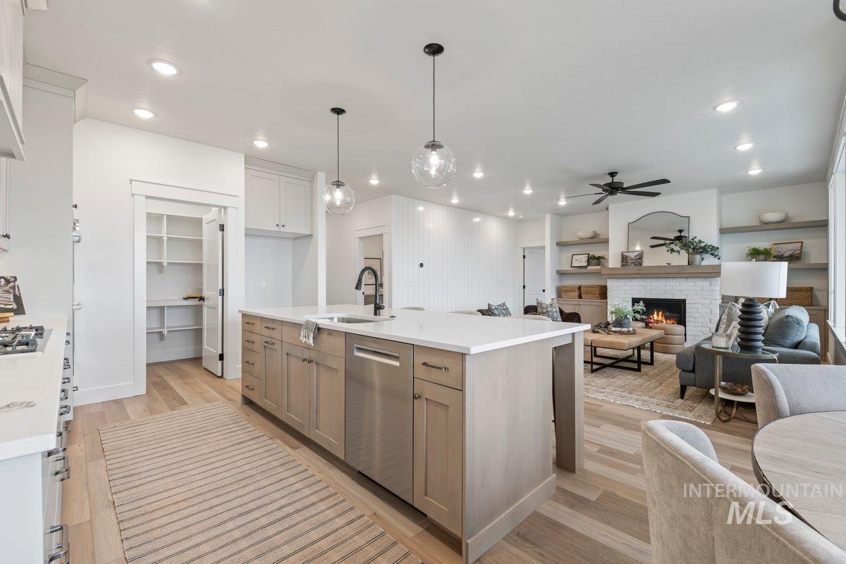 Kitchen with open floor plan, light wood-type flooring, a warm lit fireplace, stainless steel appliances, and hanging light fixtures