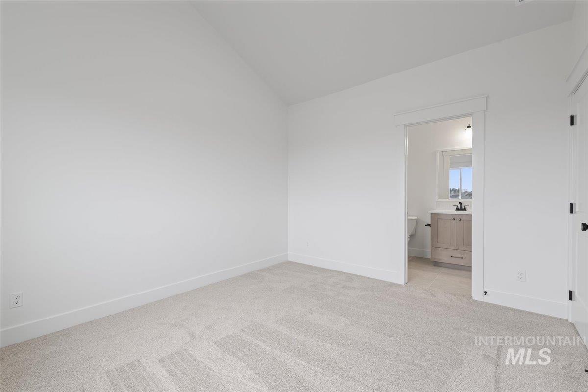 Unfurnished bedroom with lofted ceiling, light colored carpet, and ensuite bath