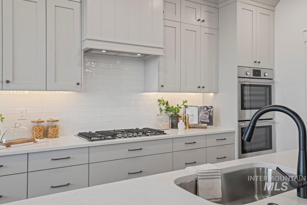Kitchen with appliances with stainless steel finishes, decorative backsplash, white cabinets, light stone countertops, and custom exhaust hood