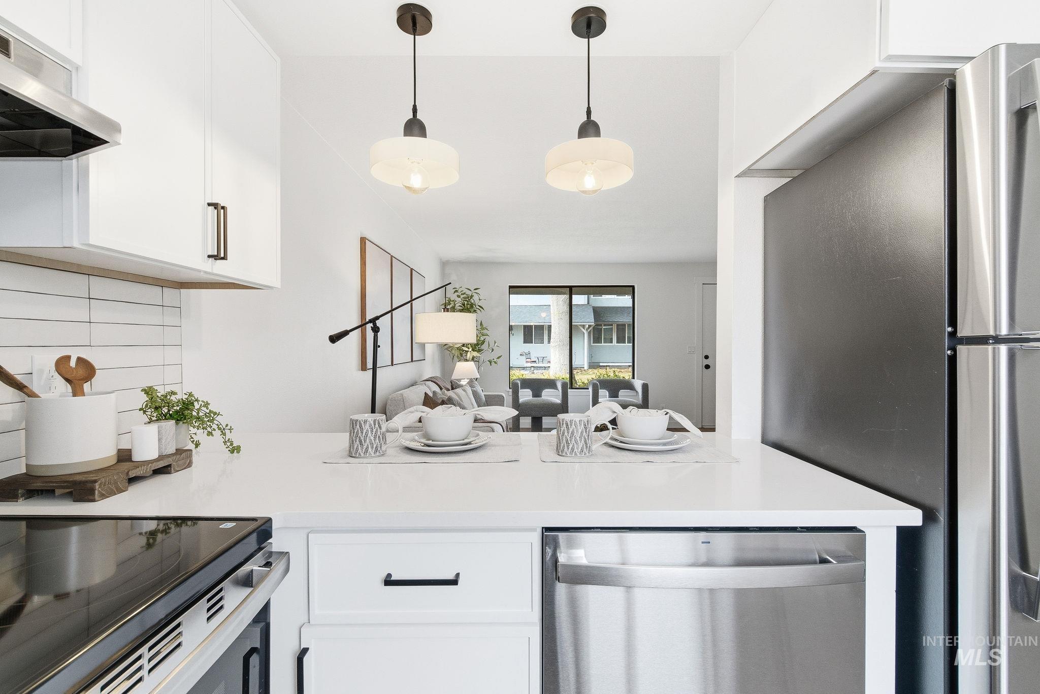 Kitchen with stainless steel appliances, tasteful backsplash, white cabinetry, open floor plan, and decorative light fixtures