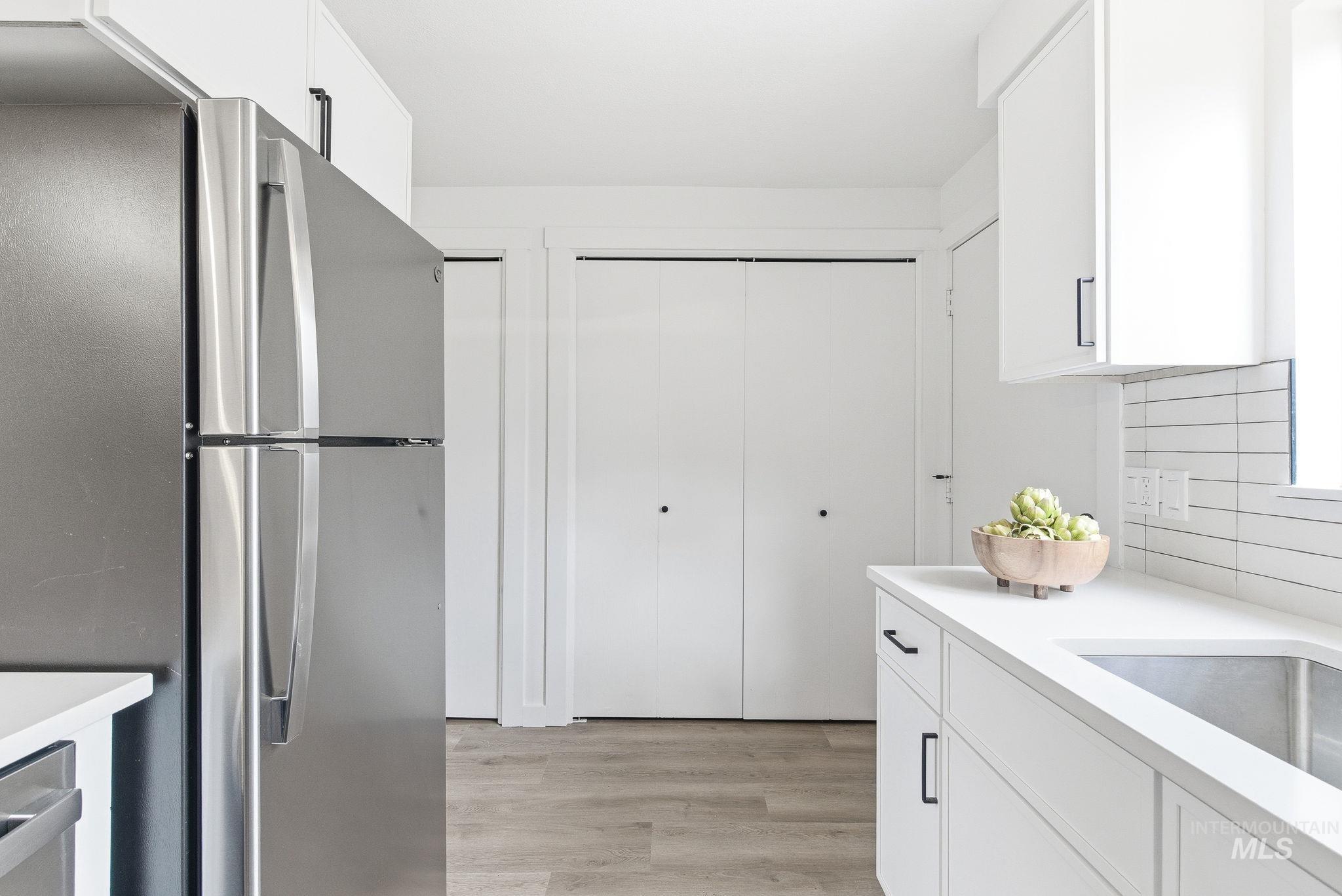 Kitchen featuring white cabinetry, freestanding refrigerator, light wood-style floors, and decorative backsplash