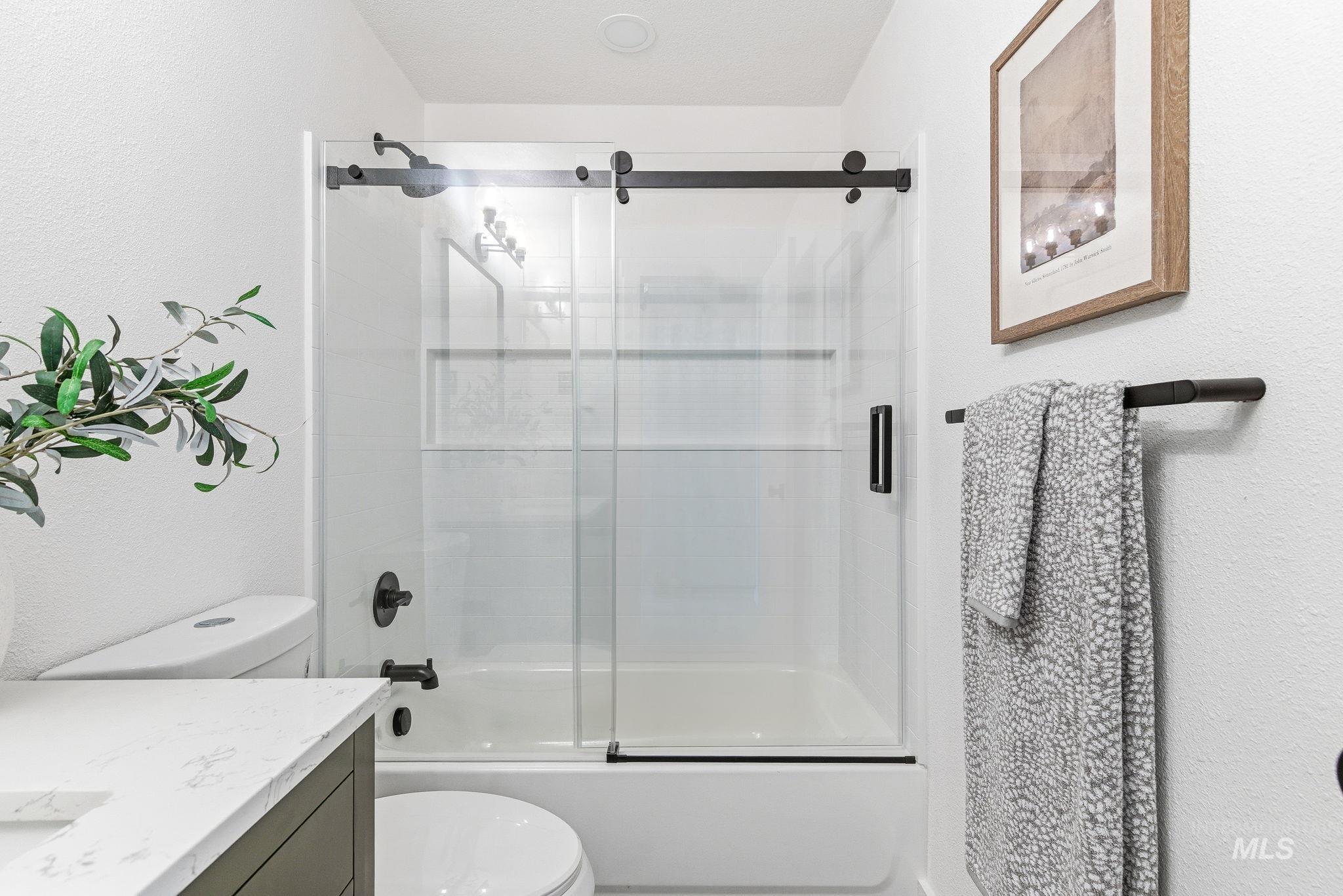 Bathroom with vanity, shower / bath combination with glass door, and a textured wall