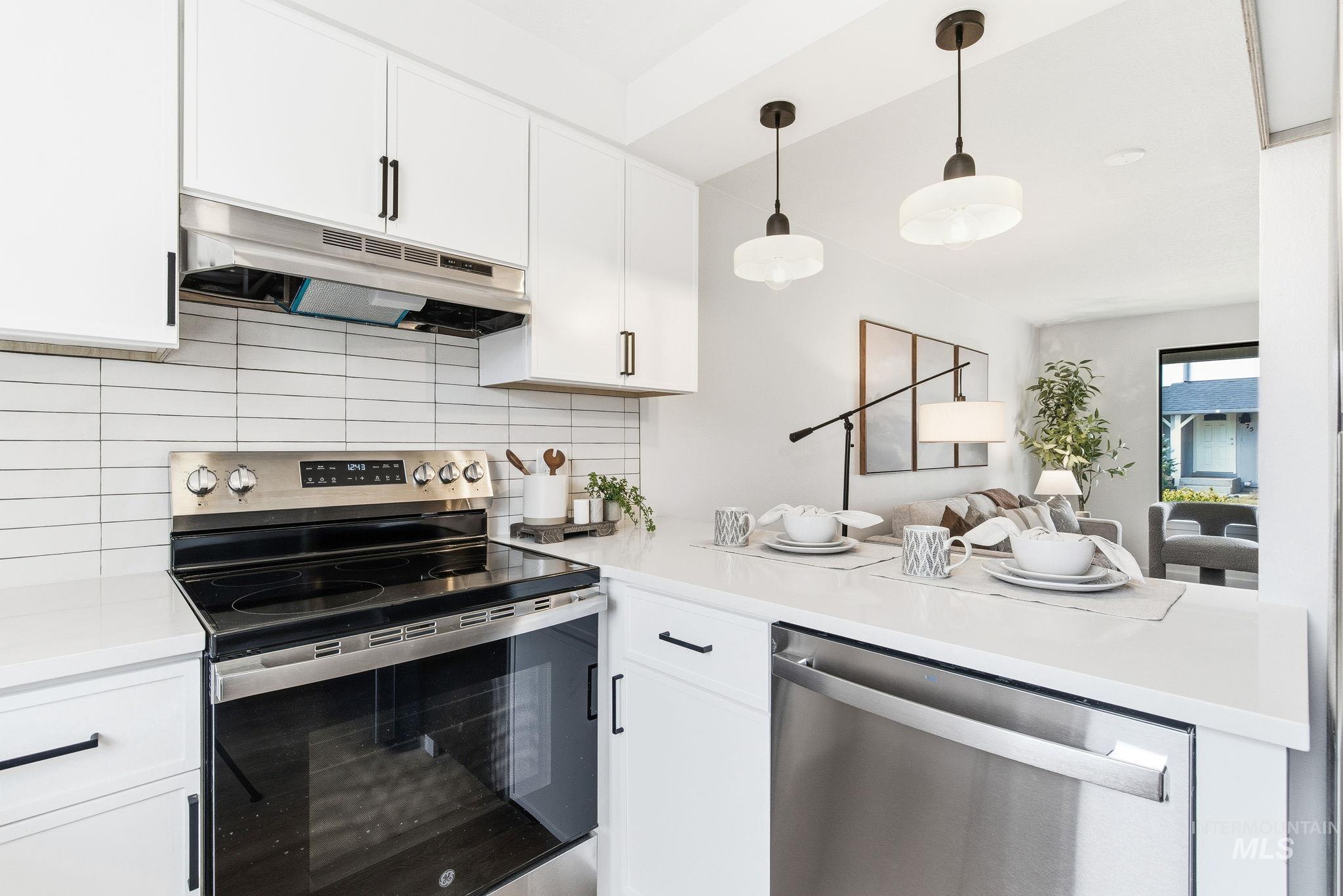 Kitchen with stainless steel appliances, white cabinets, backsplash, and decorative light fixtures