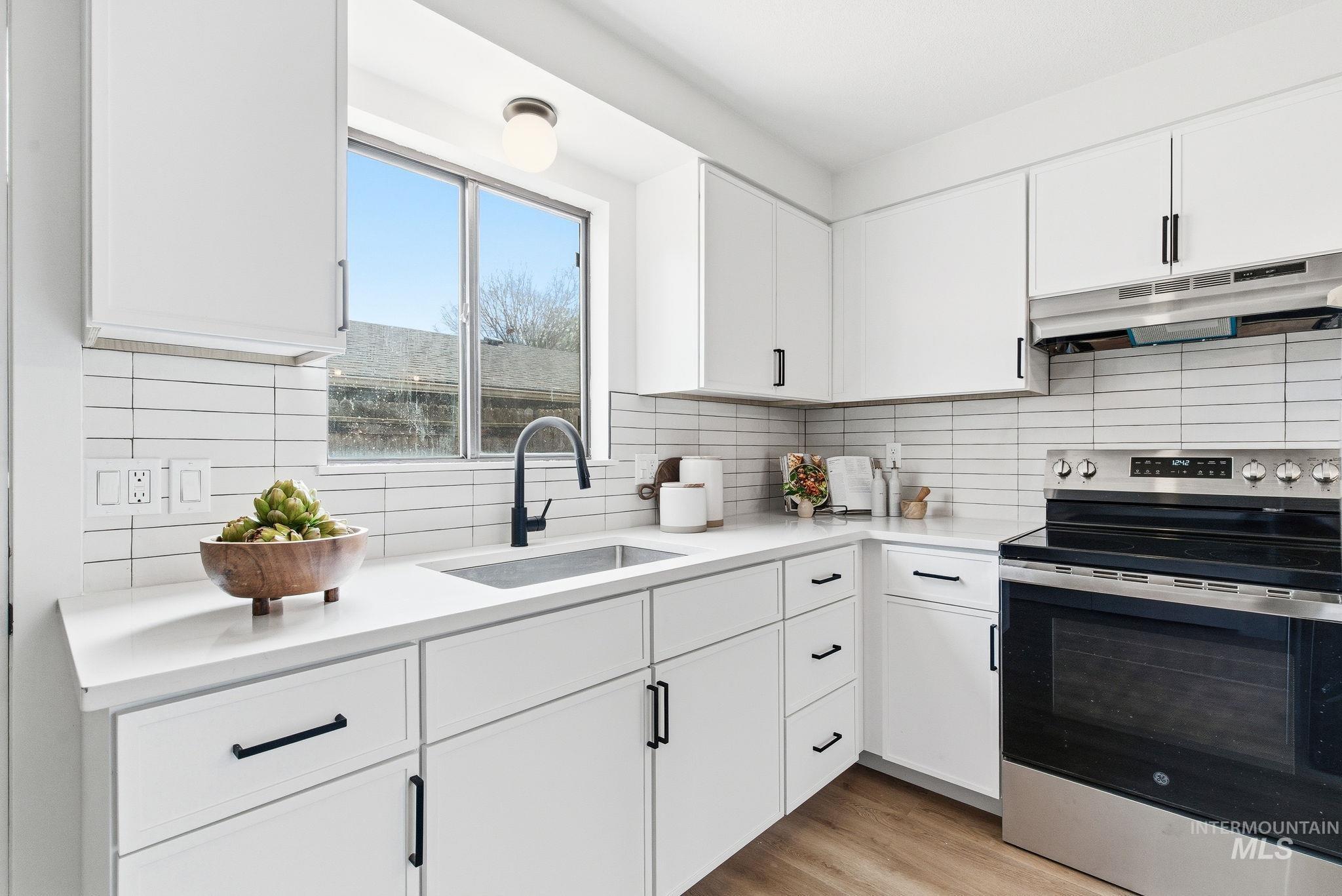 Kitchen with electric stove, white cabinetry, decorative backsplash, and light wood-type flooring