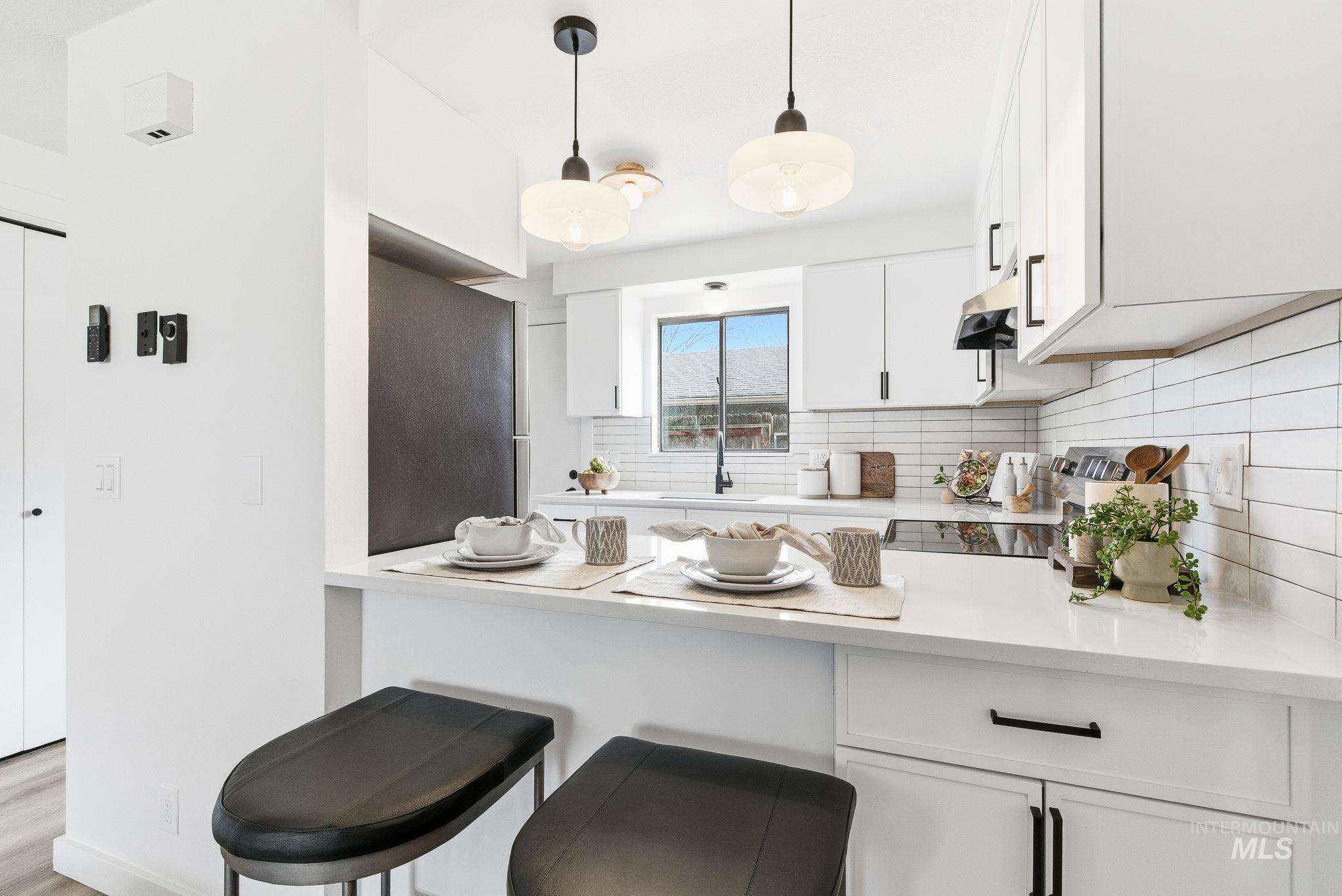 Kitchen featuring white cabinetry, a kitchen breakfast bar, a peninsula, pendant lighting, and decorative backsplash