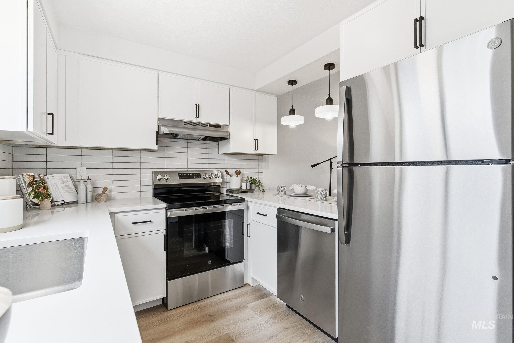 Kitchen with stainless steel appliances, hanging light fixtures, white cabinets, and light wood finished floors