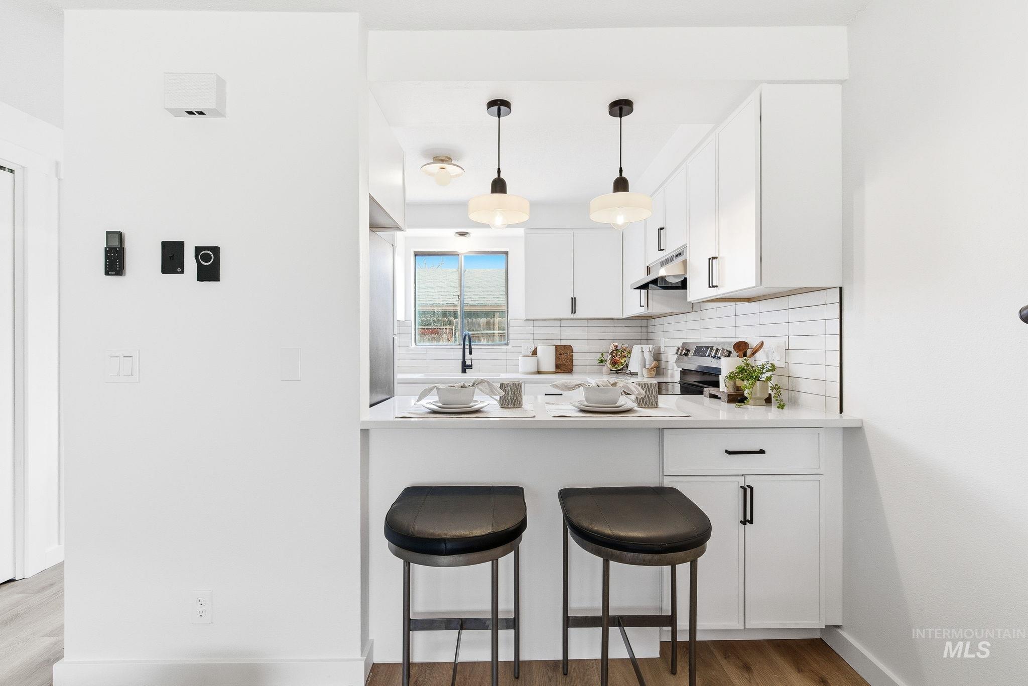 Kitchen with white cabinets, backsplash, light wood-style floors, pendant lighting, and a kitchen bar