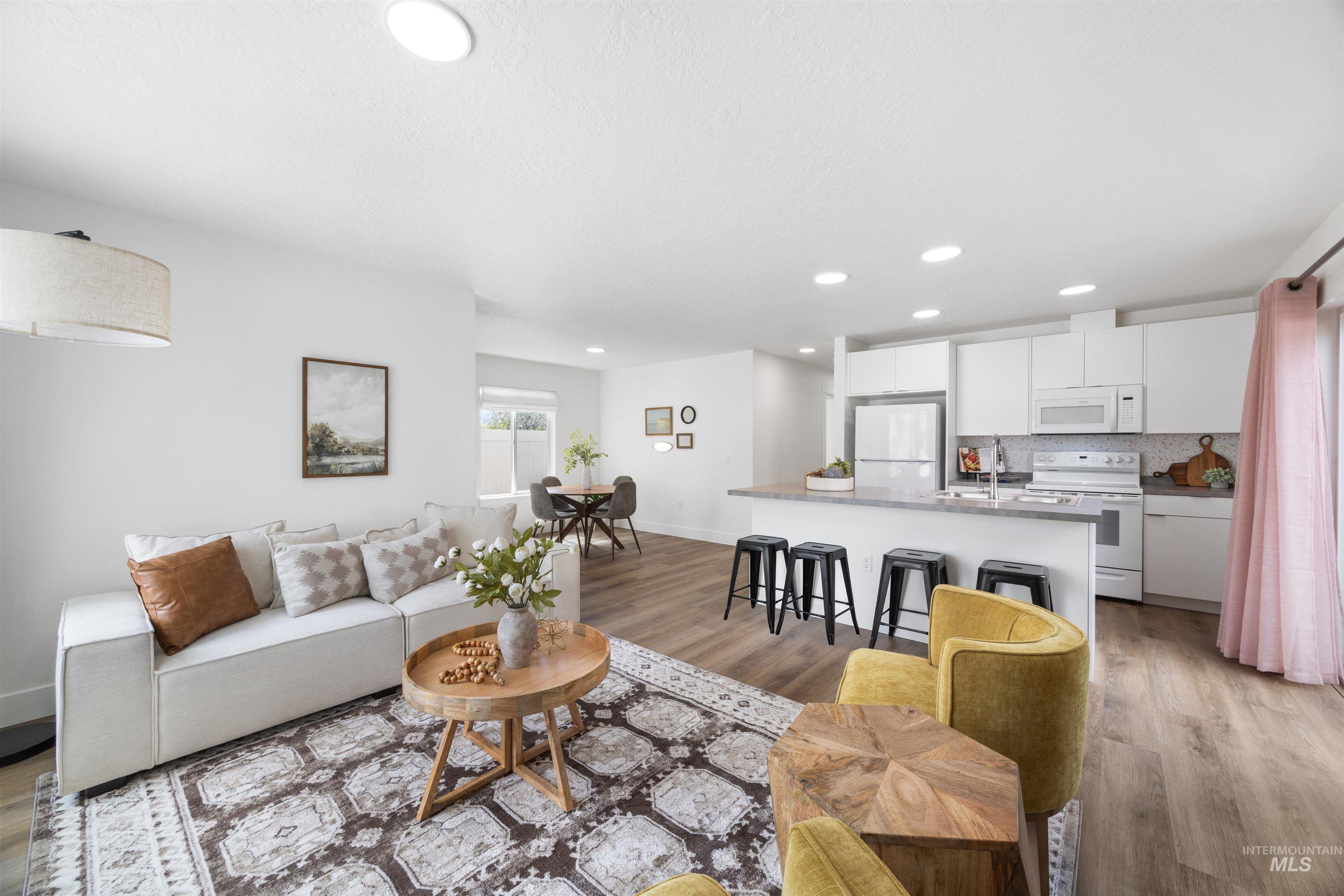 Open-concept living space featuring wood-finish flooring, recessed lighting, a kitchen island with seating, white shaker-style cabinetry, and a subway tile backsplash