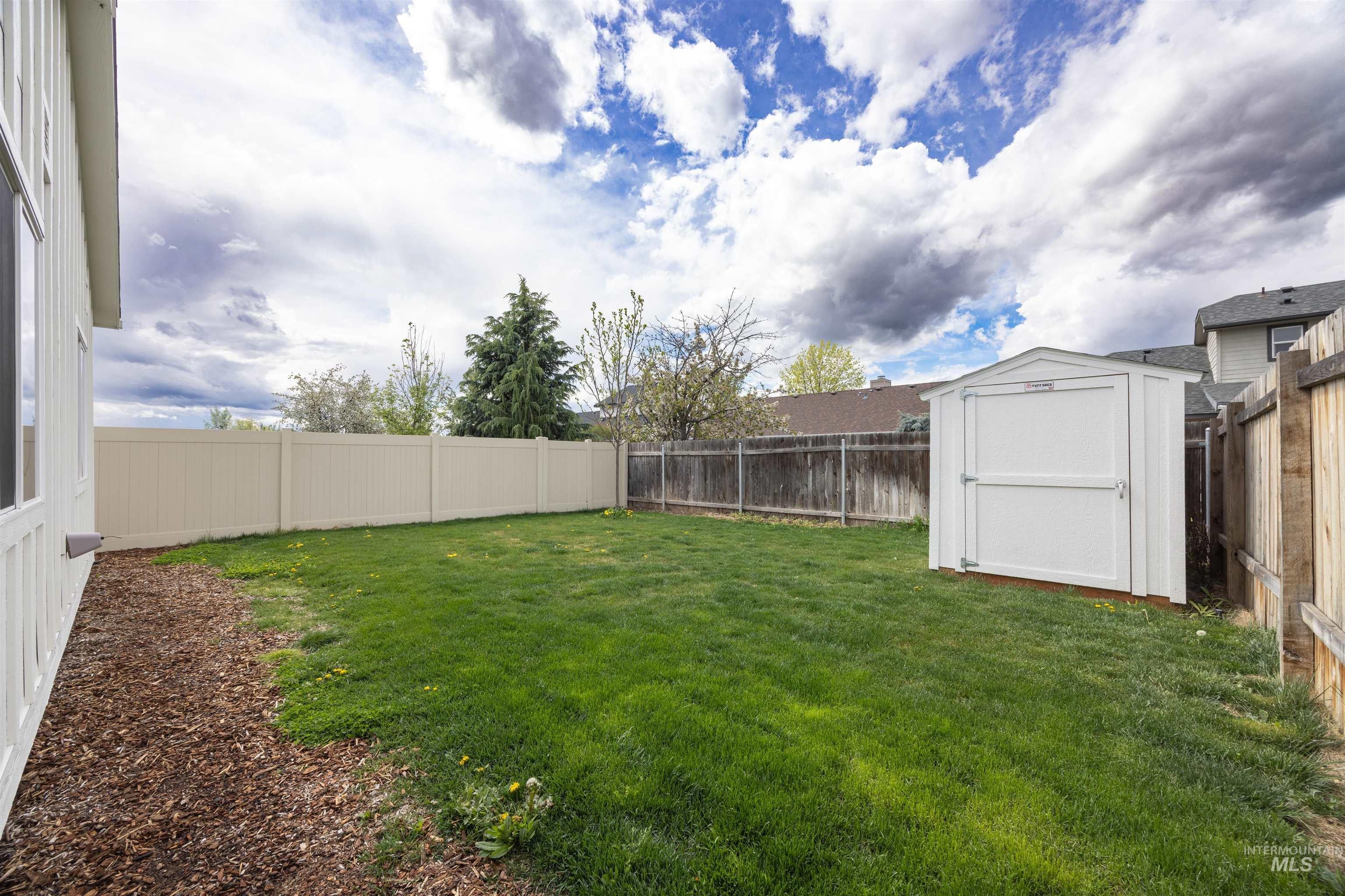 Expansive backyard featuring a lush lawn, white vinyl privacy fencing, and a dedicated storage shed