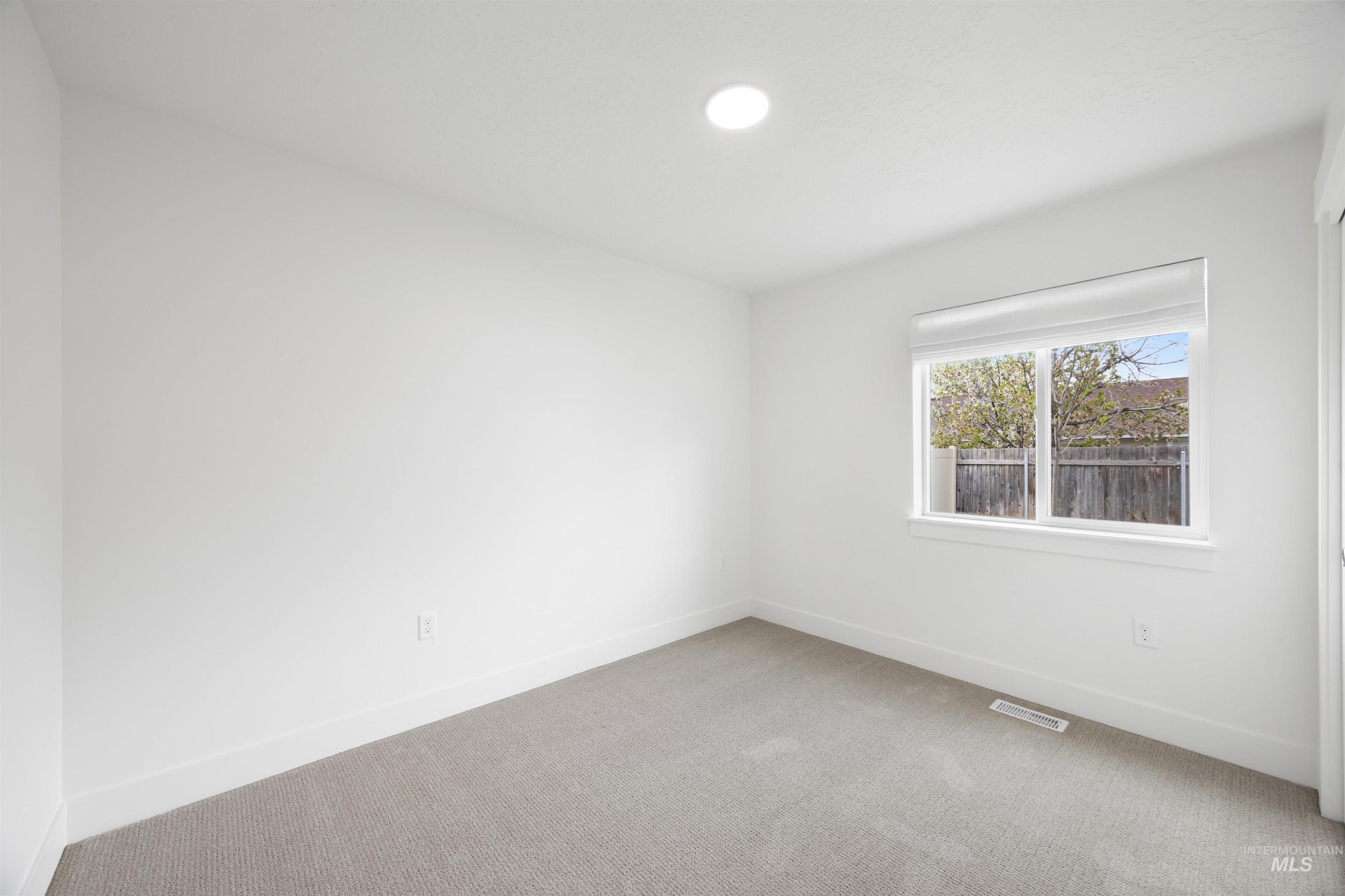 Room featuring light-colored carpeting, white walls, and a single window with a roller shade
