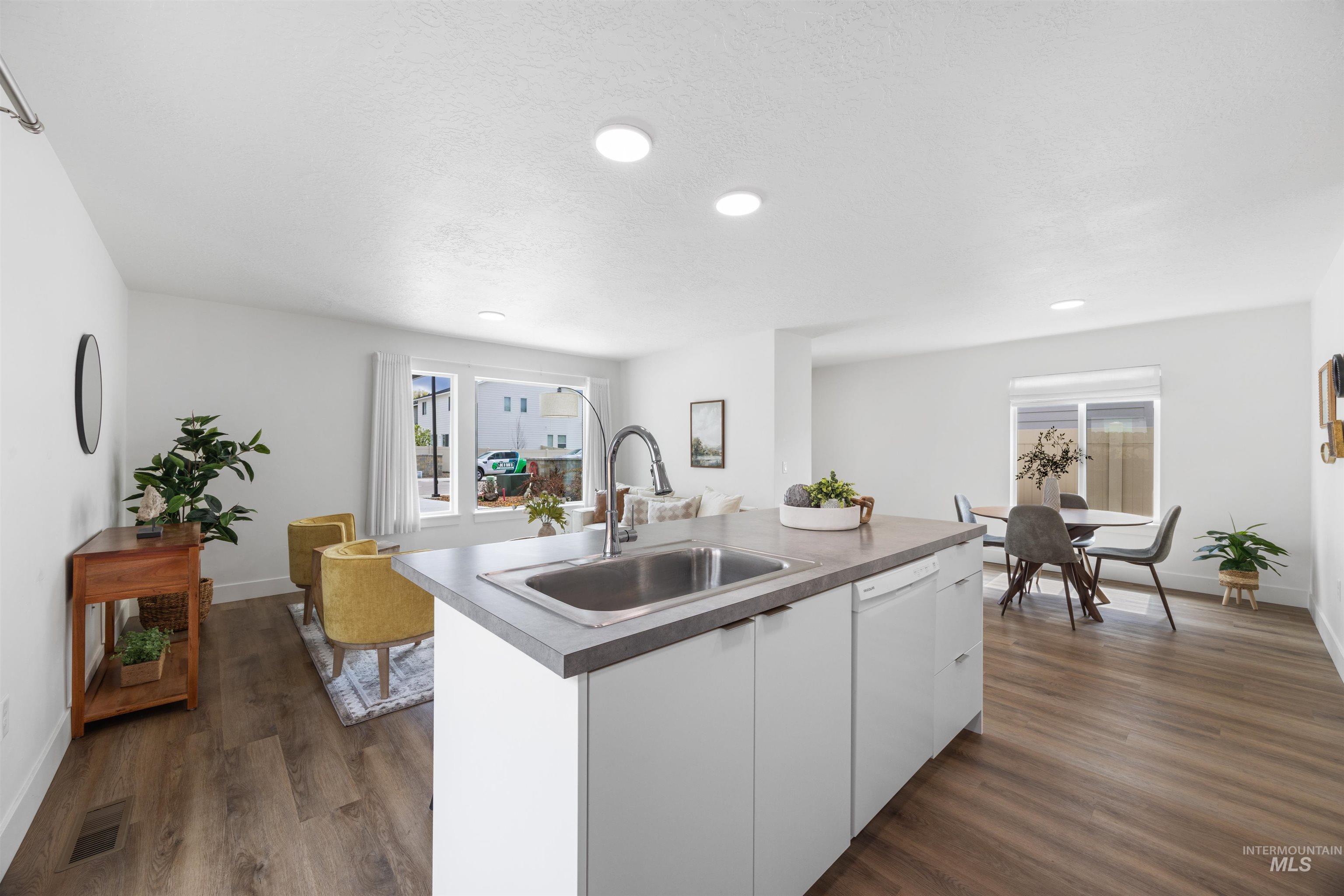 Kitchen island with an undermount sink and integrated dishwasher, surrounded by light wood-finish flooring