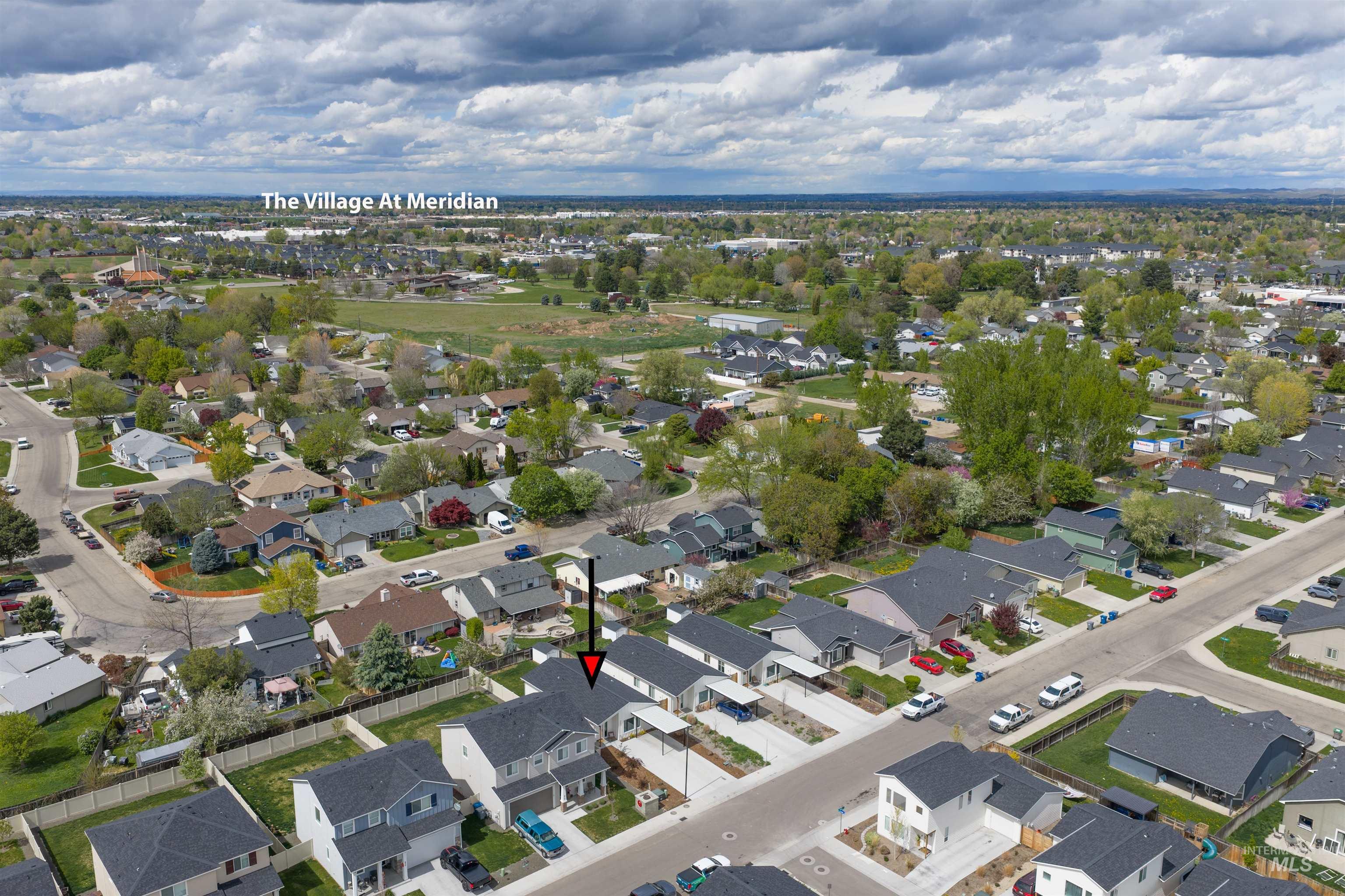 Aerial perspective of a neighborhood featuring residential properties with dark-shingled roofs, green lawns, and mature trees