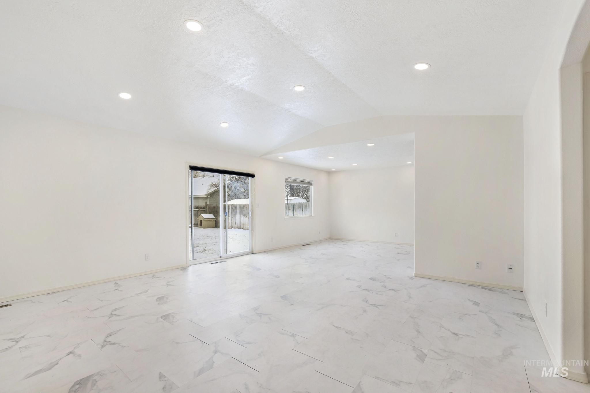 Empty room featuring vaulted ceiling, light marble finish floors, and recessed lighting