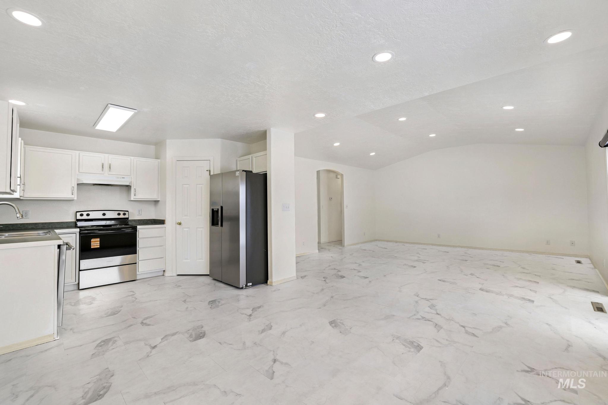 Kitchen with appliances with stainless steel finishes, white cabinets, arched walkways, open floor plan, and under cabinet range hood