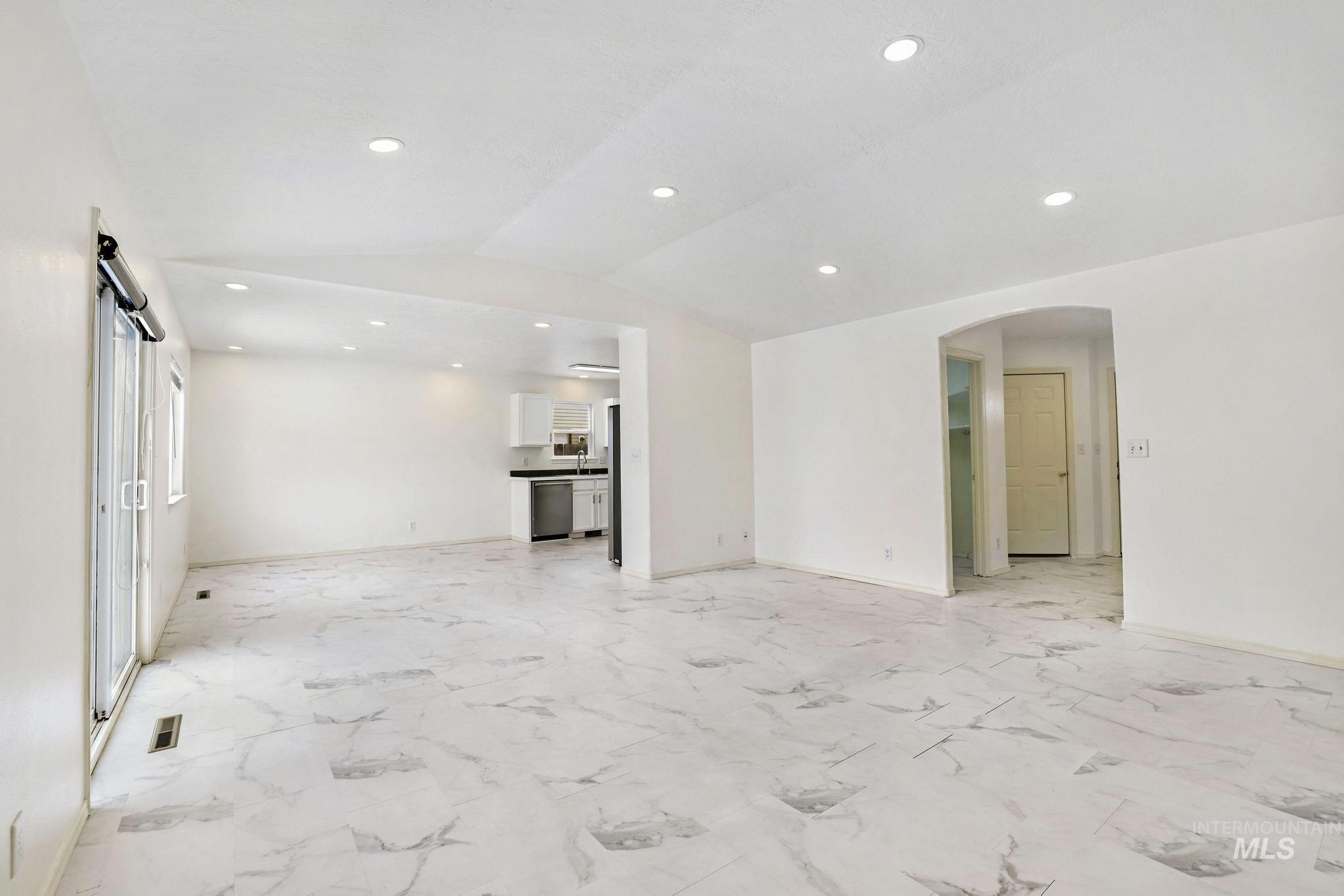 Unfurnished living room with arched walkways, lofted ceiling, light marble finish flooring, and recessed lighting