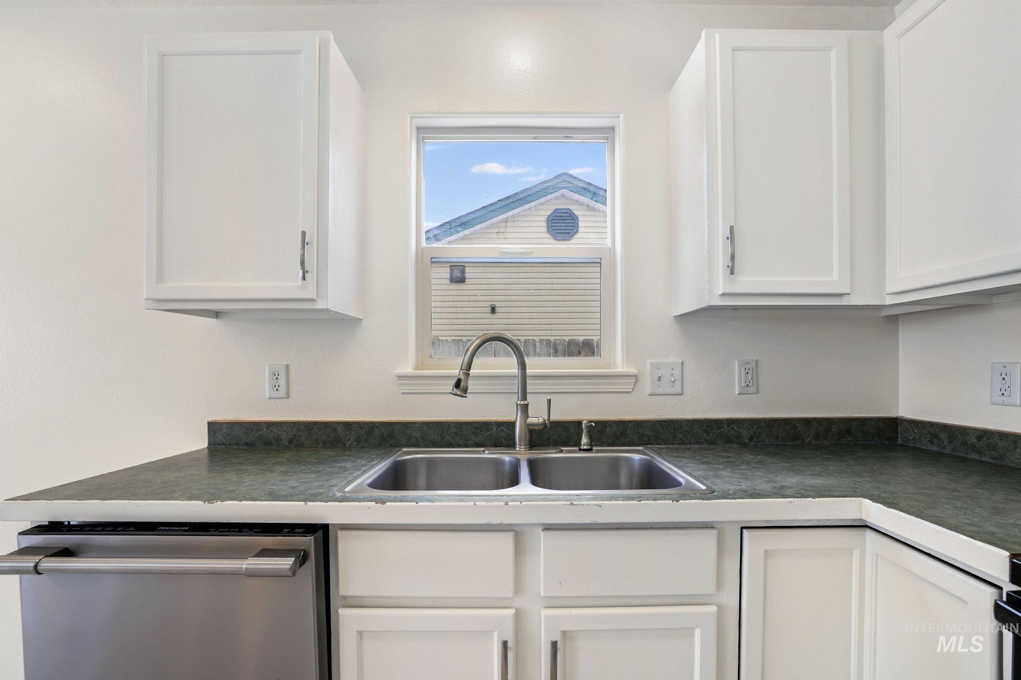 Kitchen featuring dark countertops, stainless steel dishwasher, and white cabinetry
