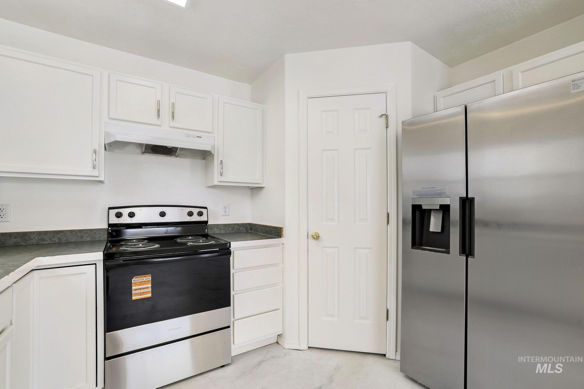 Kitchen featuring stainless steel appliances, white cabinetry, under cabinet range hood, and light marble finish floors