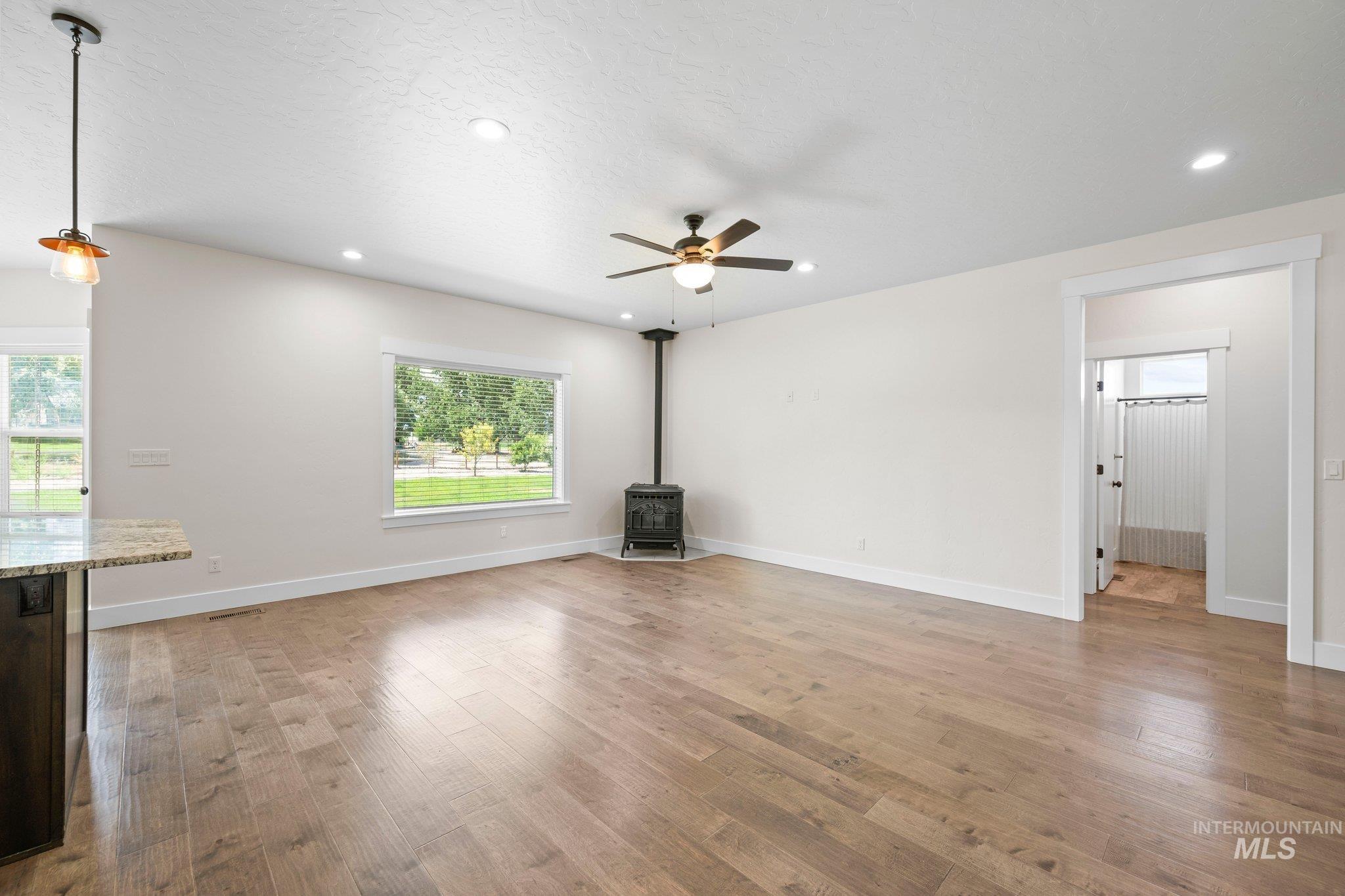 Unfurnished living room with a wood stove, ceiling fan, plenty of natural light, light wood-style floors, and recessed lighting