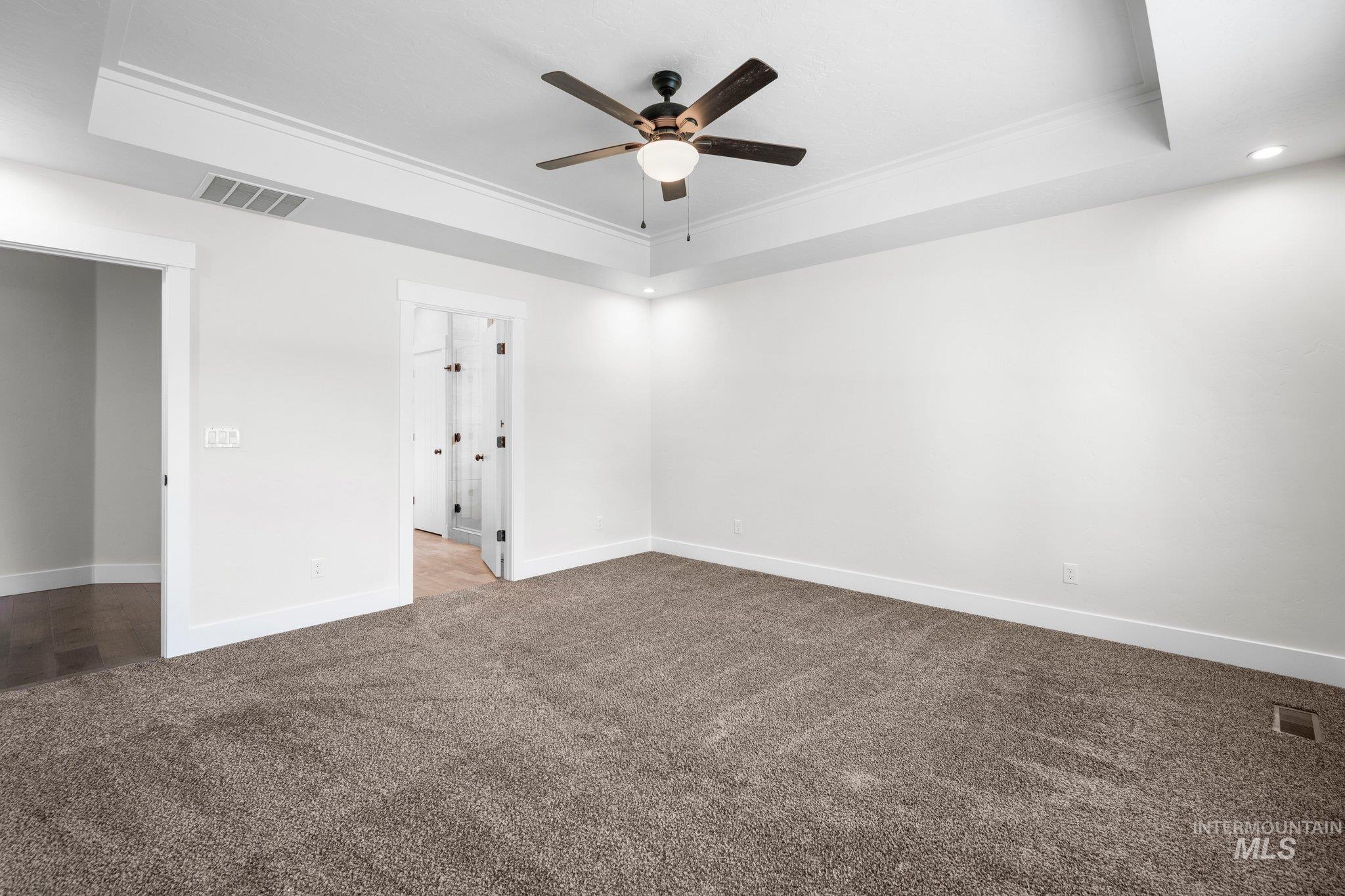 Carpeted empty room with a raised ceiling, a ceiling fan, ornamental molding, and recessed lighting