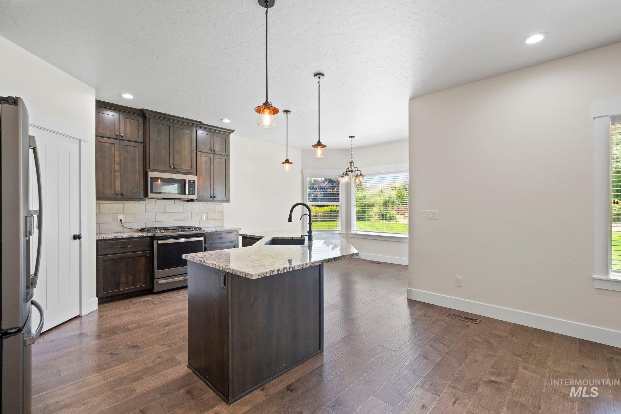Kitchen featuring stainless steel appliances, dark brown cabinetry, tasteful backsplash, light stone countertops, and recessed lighting