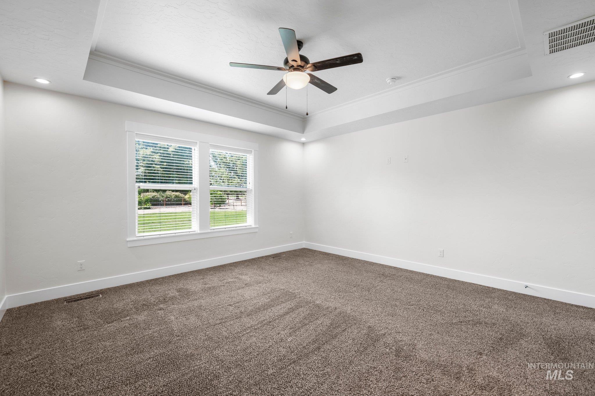 Empty room with a raised ceiling, ornamental molding, ceiling fan, carpet floors, and recessed lighting