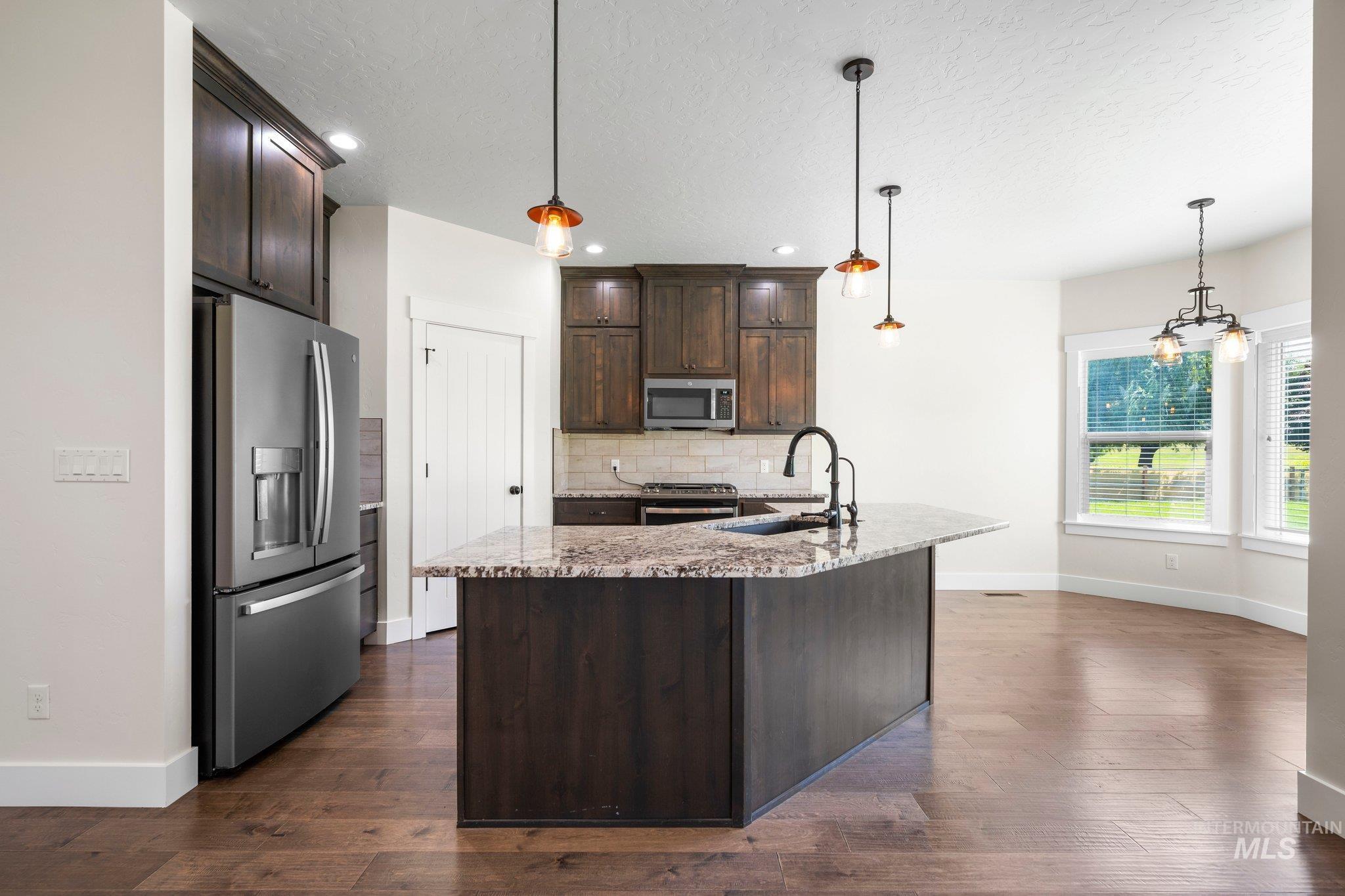 Kitchen with appliances with stainless steel finishes, dark brown cabinetry, decorative backsplash, dark wood-style flooring, and a textured ceiling