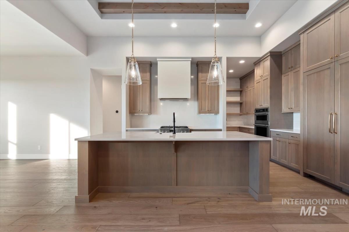 Kitchen with a spacious island, open shelves, pendant lighting, custom range hood, and light wood-type flooring