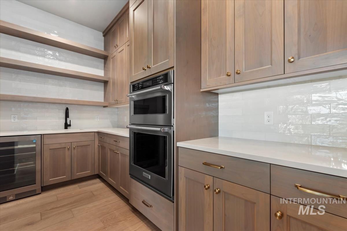 Kitchen with open shelves, stainless steel double oven, beverage cooler, and backsplash