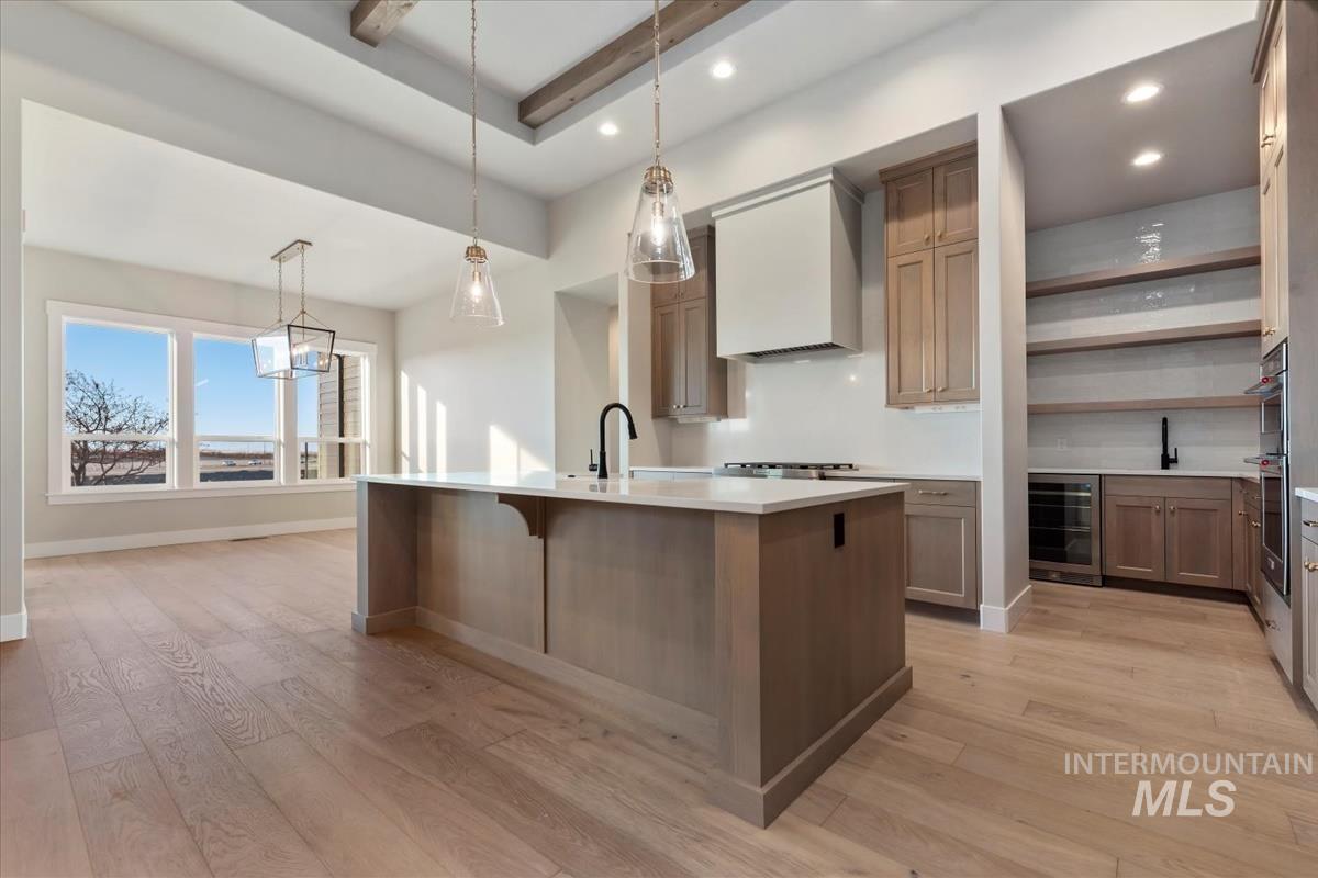Kitchen with hanging light fixtures, open shelves, a kitchen island with sink, light wood-style floors, and recessed lighting