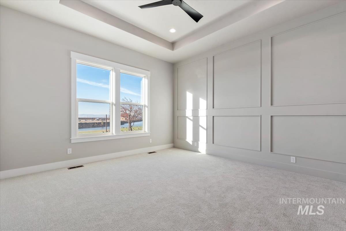 Carpeted empty room featuring a decorative wall, a raised ceiling, and recessed lighting