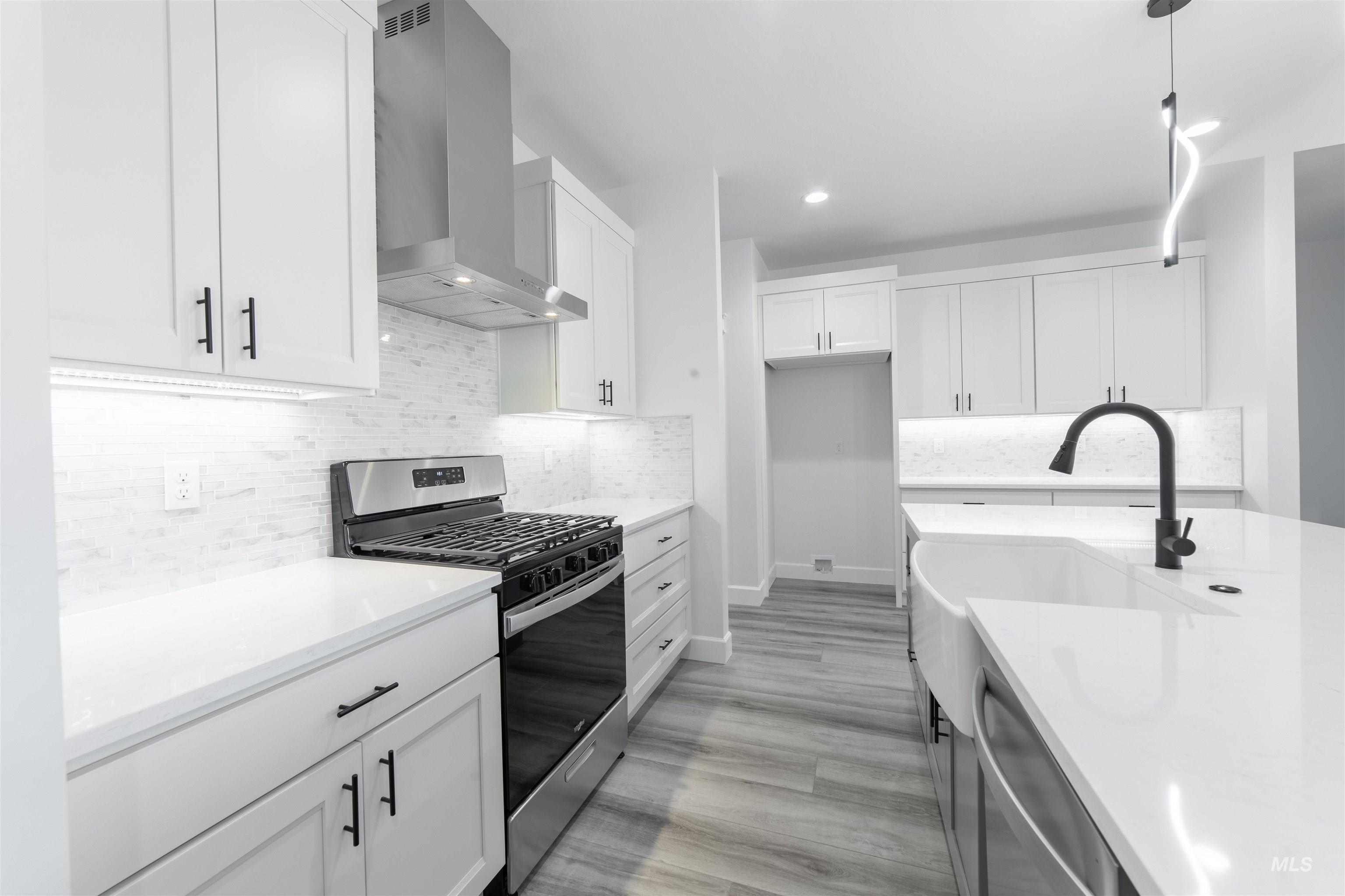 Kitchen with stainless steel appliances, wall chimney range hood, light wood-style flooring, white cabinetry, and decorative backsplash