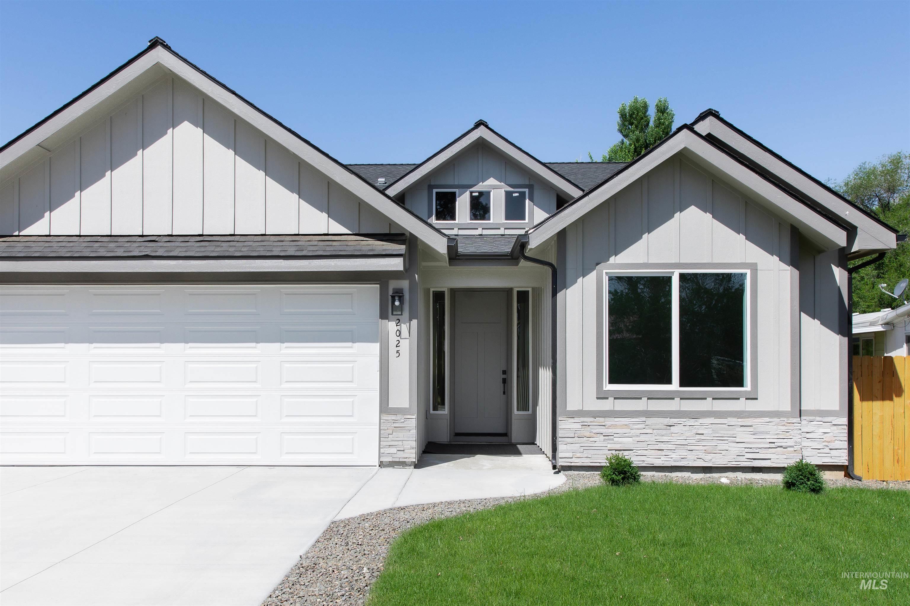 View of front of home with board and batten siding, stone siding, roof with shingles, and driveway