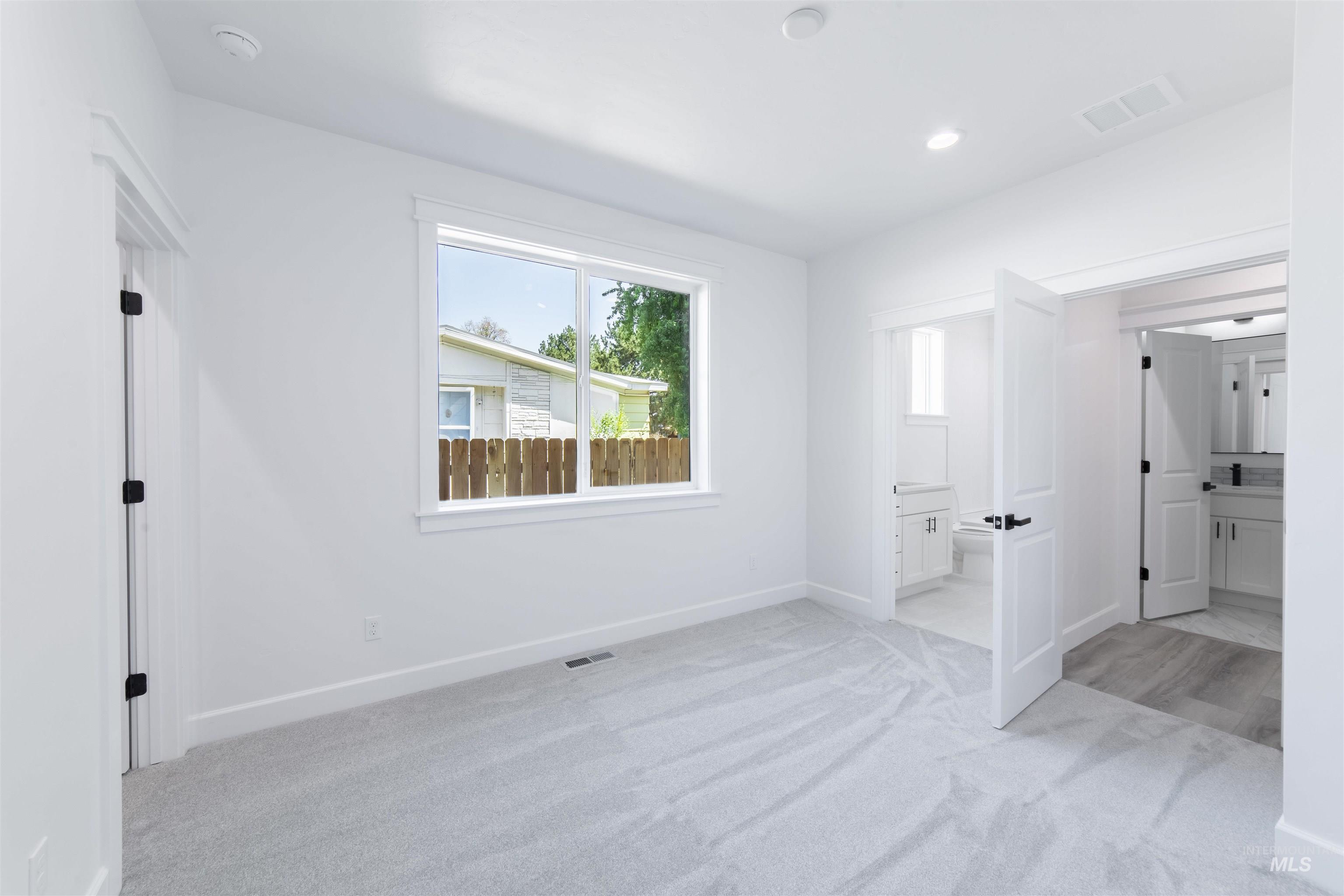 Unfurnished bedroom with multiple windows, light colored carpet, ensuite bath, and recessed lighting
