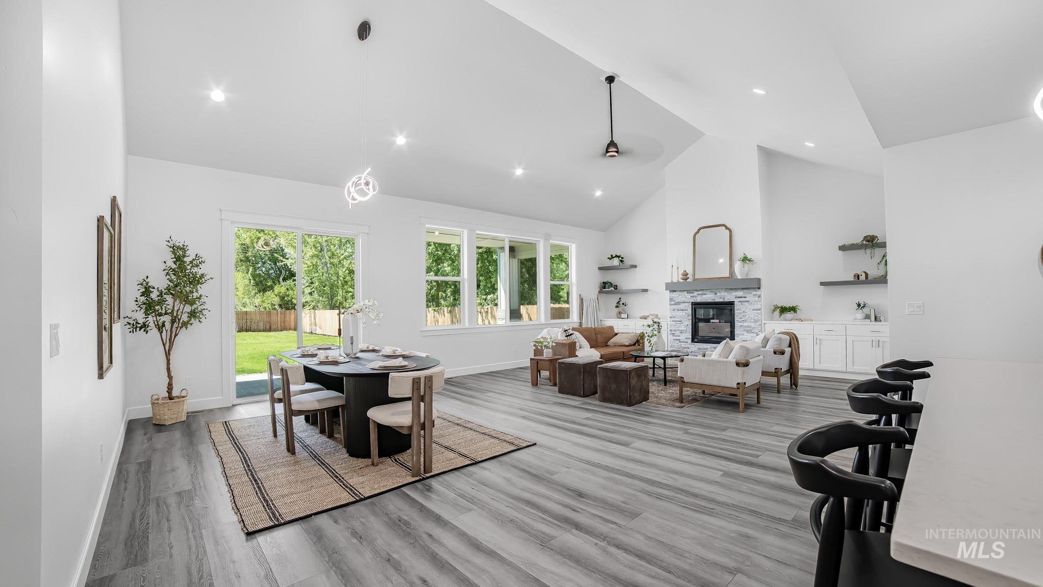 Dining area with high vaulted ceiling, wood finished floors, a stone fireplace, and recessed lighting