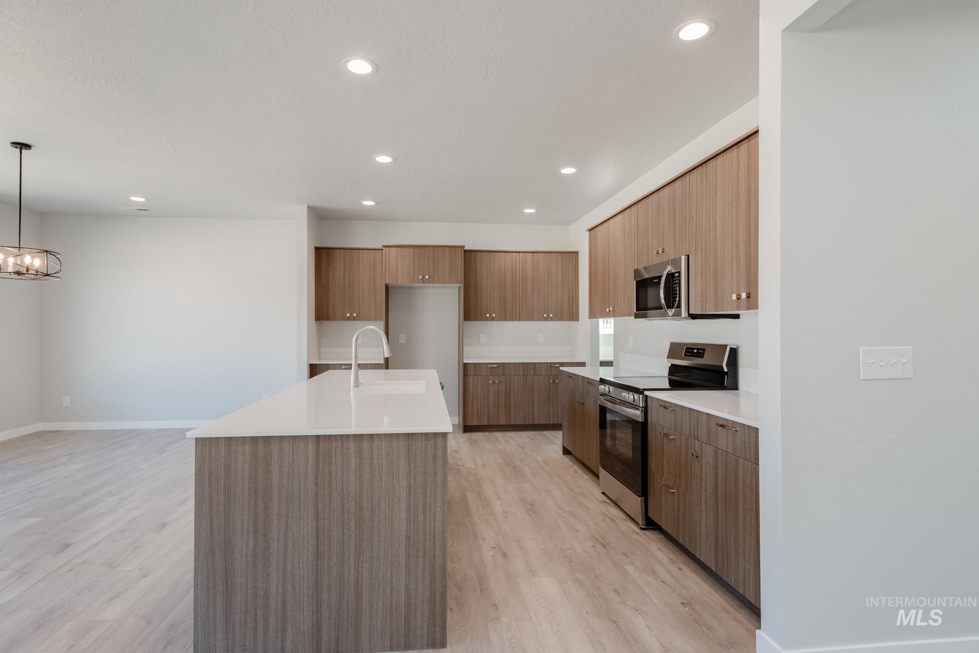 Kitchen with appliances with stainless steel finishes, modern cabinets, light wood-style flooring, a center island with sink, and pendant lighting