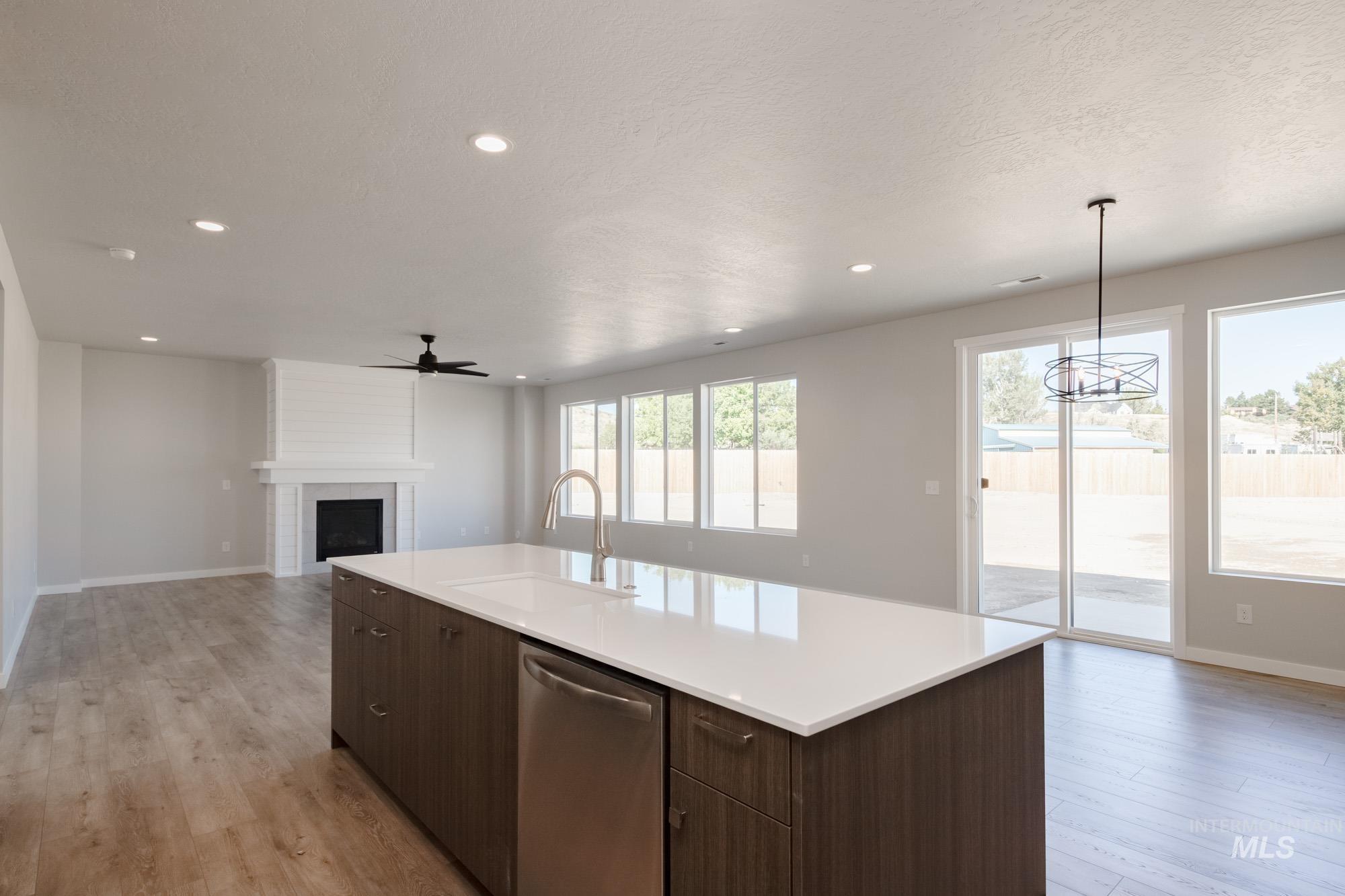 Kitchen with dark brown cabinets, open floor plan, dishwasher, a large fireplace, and light wood-style flooring