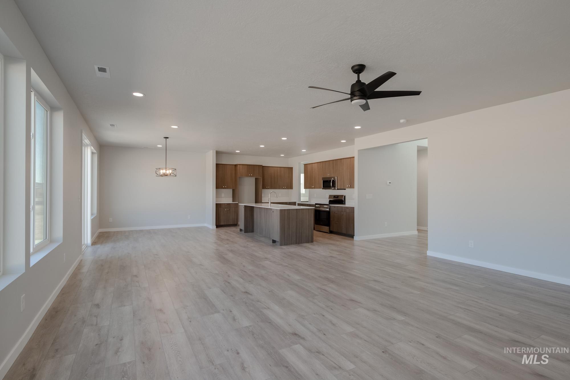 Unfurnished living room with recessed lighting, light wood-style flooring, ceiling fan, and a chandelier