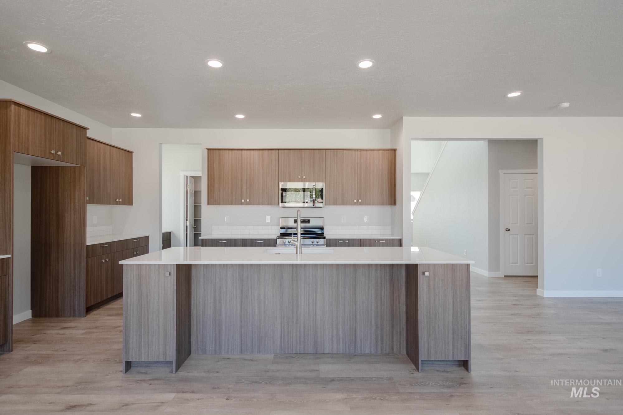Kitchen featuring modern cabinets, an island with sink, appliances with stainless steel finishes, light stone counters, and recessed lighting