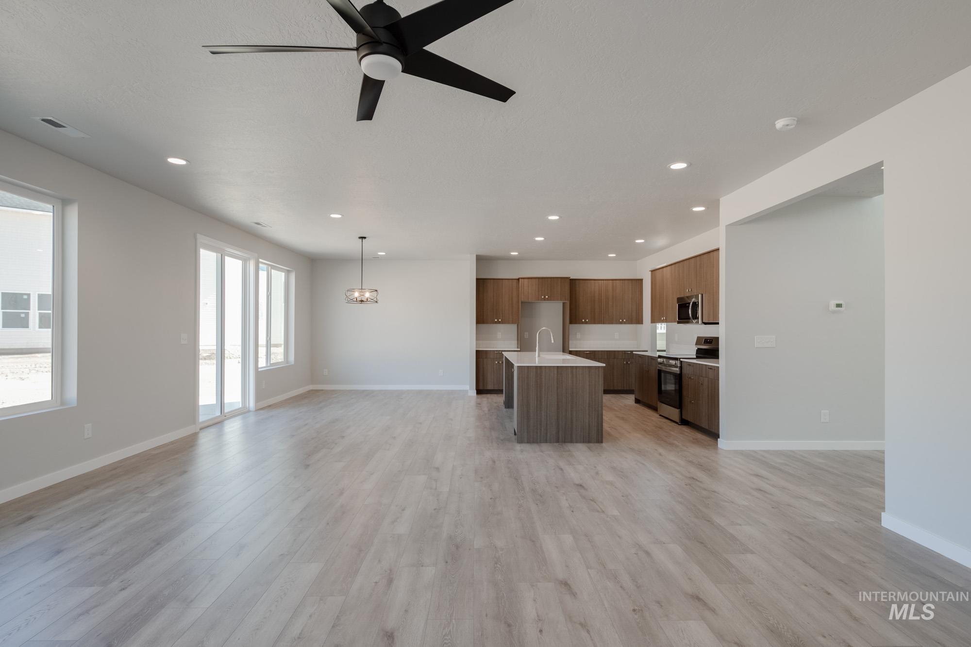 Unfurnished living room with a ceiling fan, recessed lighting, light wood finished floors, and a chandelier
