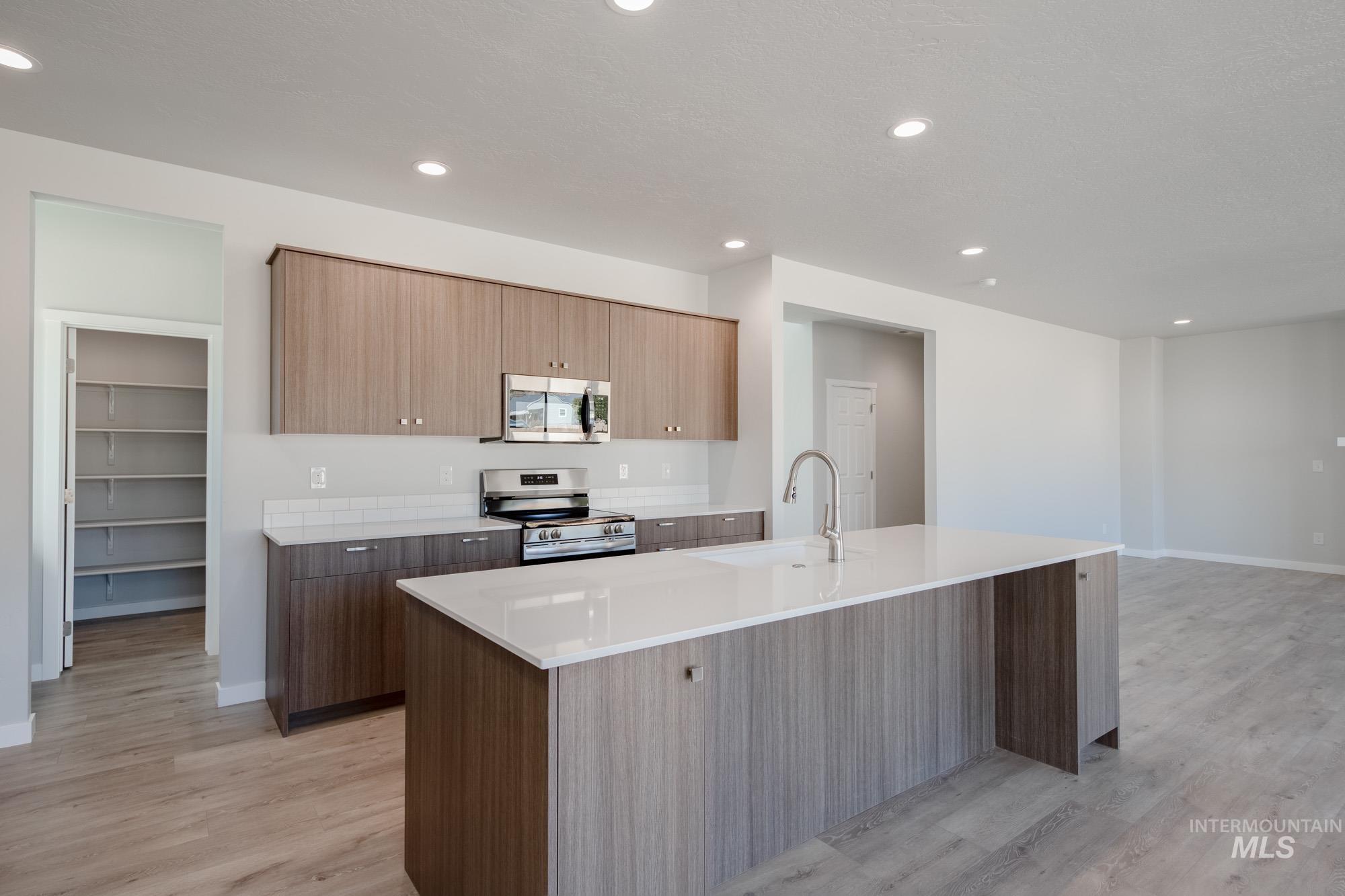 Kitchen featuring appliances with stainless steel finishes, recessed lighting, light stone countertops, light wood finished floors, and a center island with sink