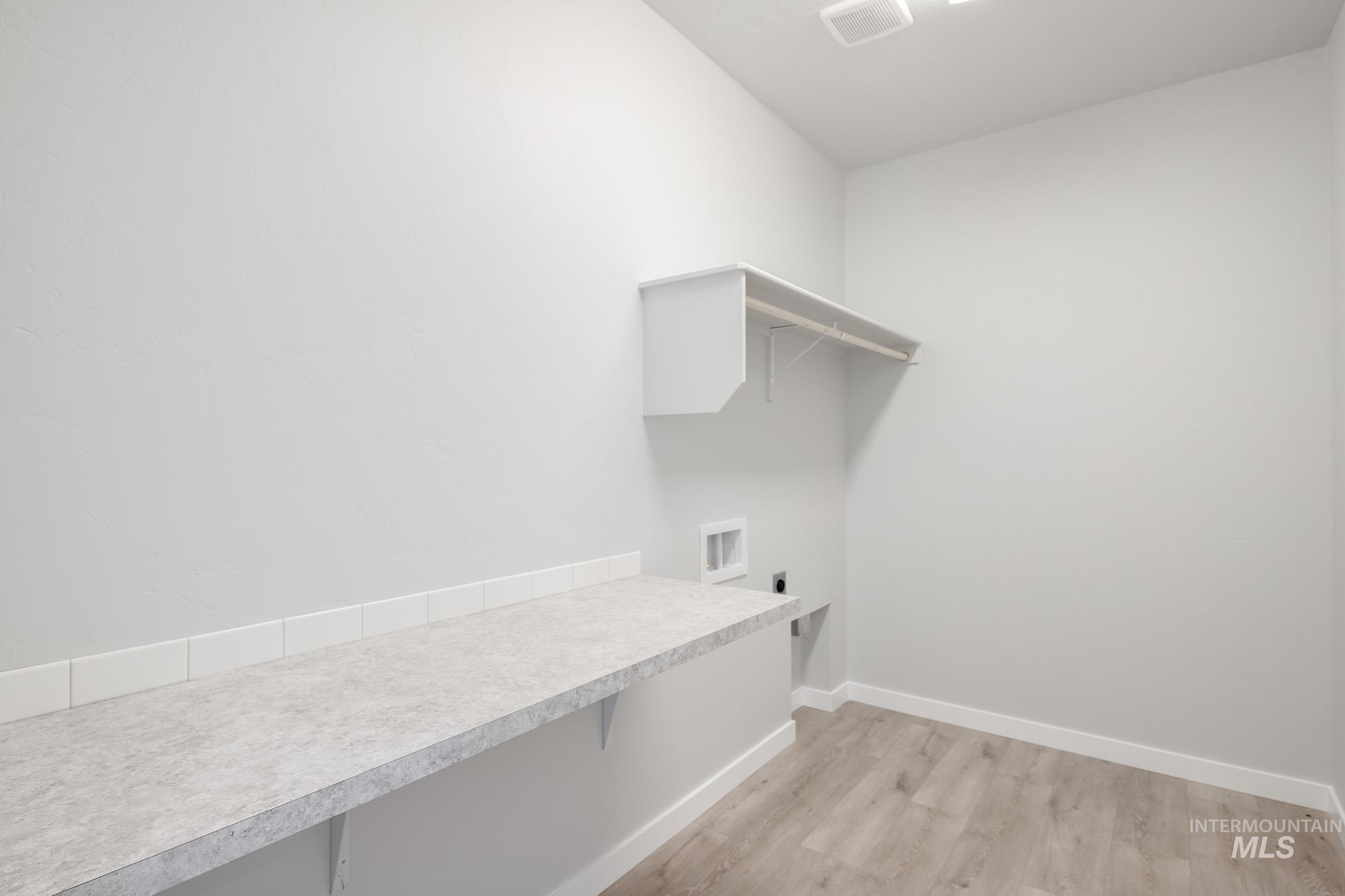 Washroom with light wood-style flooring and hookup for an electric dryer