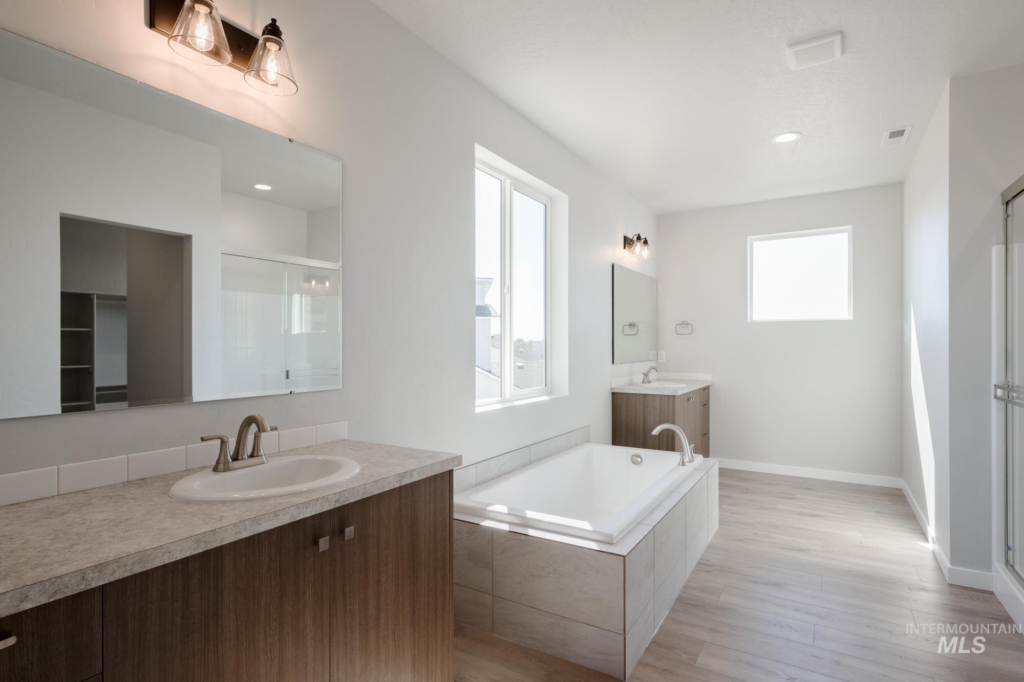 Full bath featuring two vanities, healthy amount of natural light, a shower stall, a garden tub, and recessed lighting