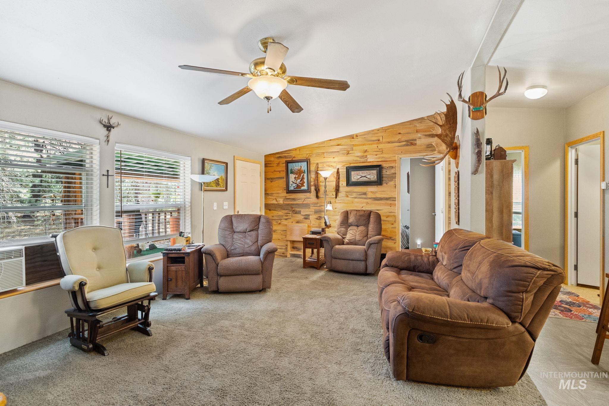 Living area featuring wooden walls, lofted ceiling, light colored carpet, and a ceiling fan