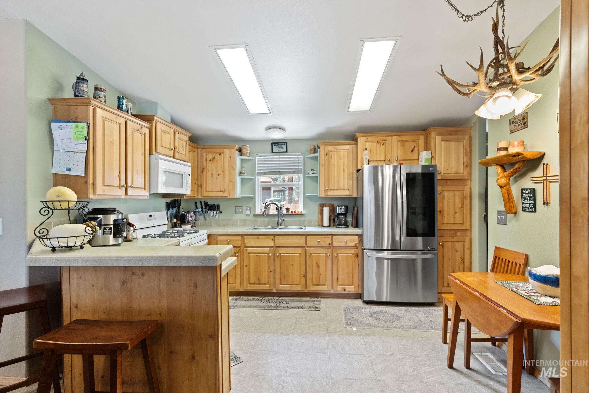 Kitchen with light countertops, white appliances, open shelves, a breakfast bar area, and a peninsula