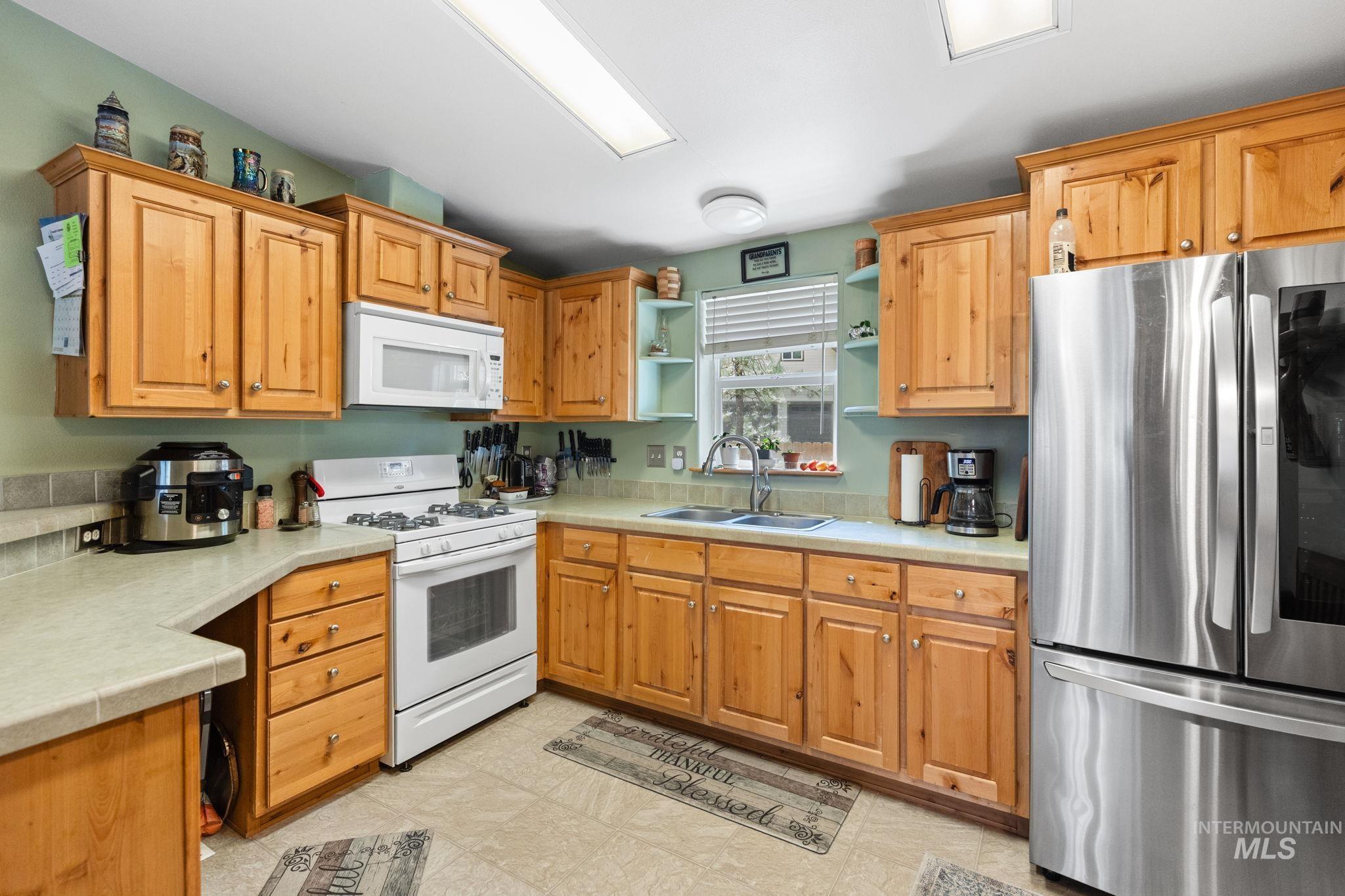 Kitchen featuring white appliances, light countertops, open shelves, and brown cabinetry