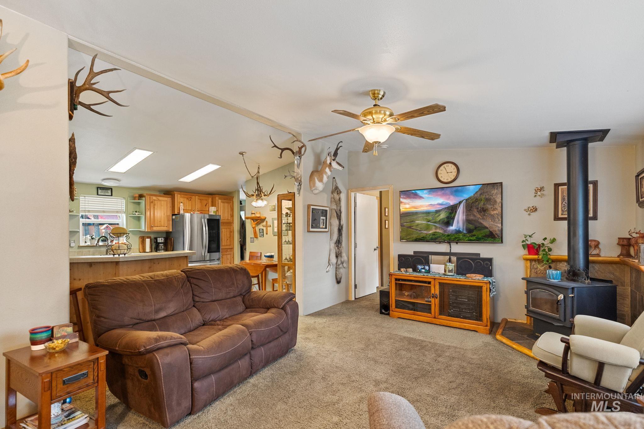 Living area with a wood stove, light carpet, lofted ceiling, and ceiling fan