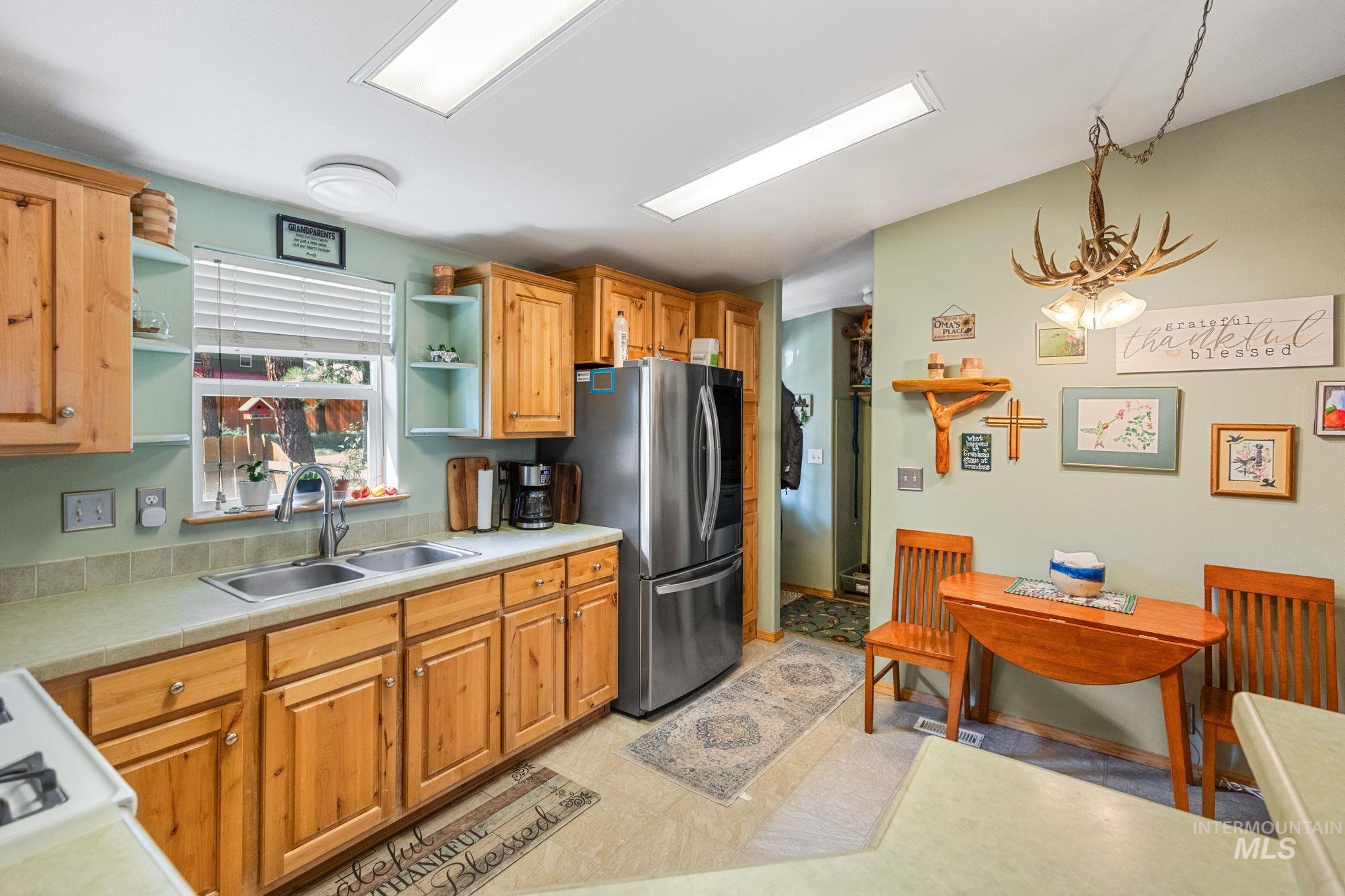 Kitchen with light countertops, a chandelier, open shelves, freestanding refrigerator, and brown cabinets