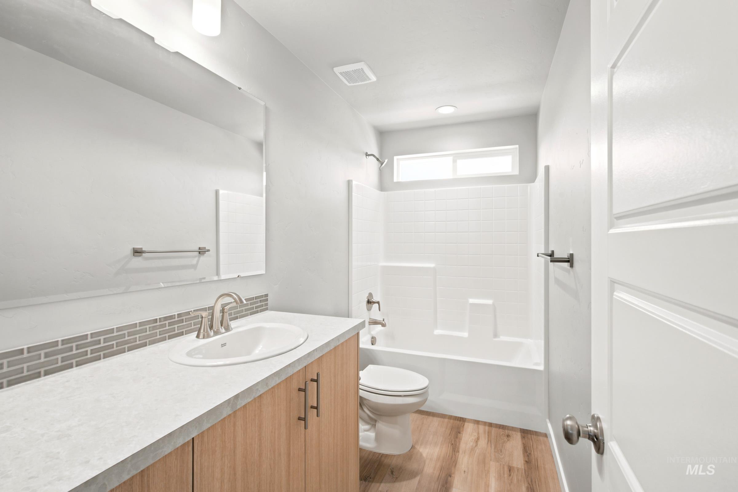 Bathroom featuring a wood-finish vanity with a single basin sink, light-colored countertop, and a mosaic tile backsplash
